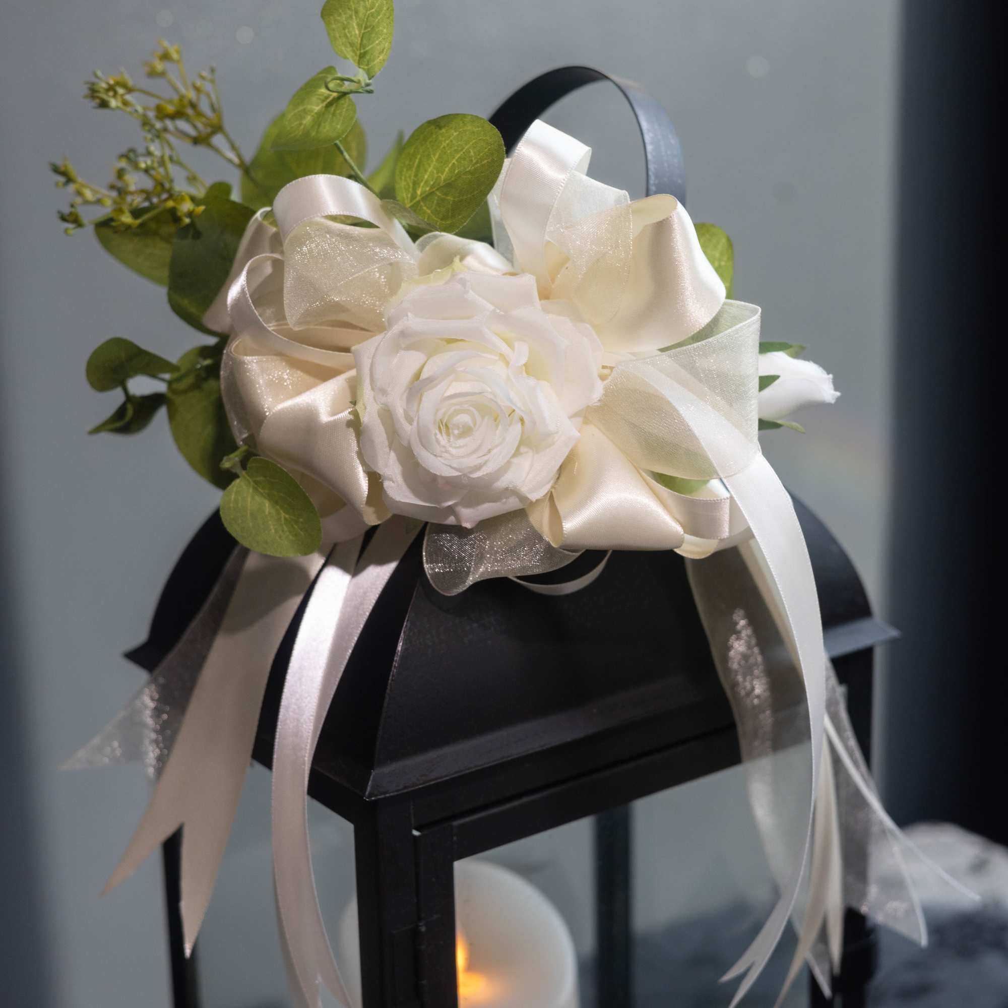 White rose arrangement with cream ribbons on a black lantern