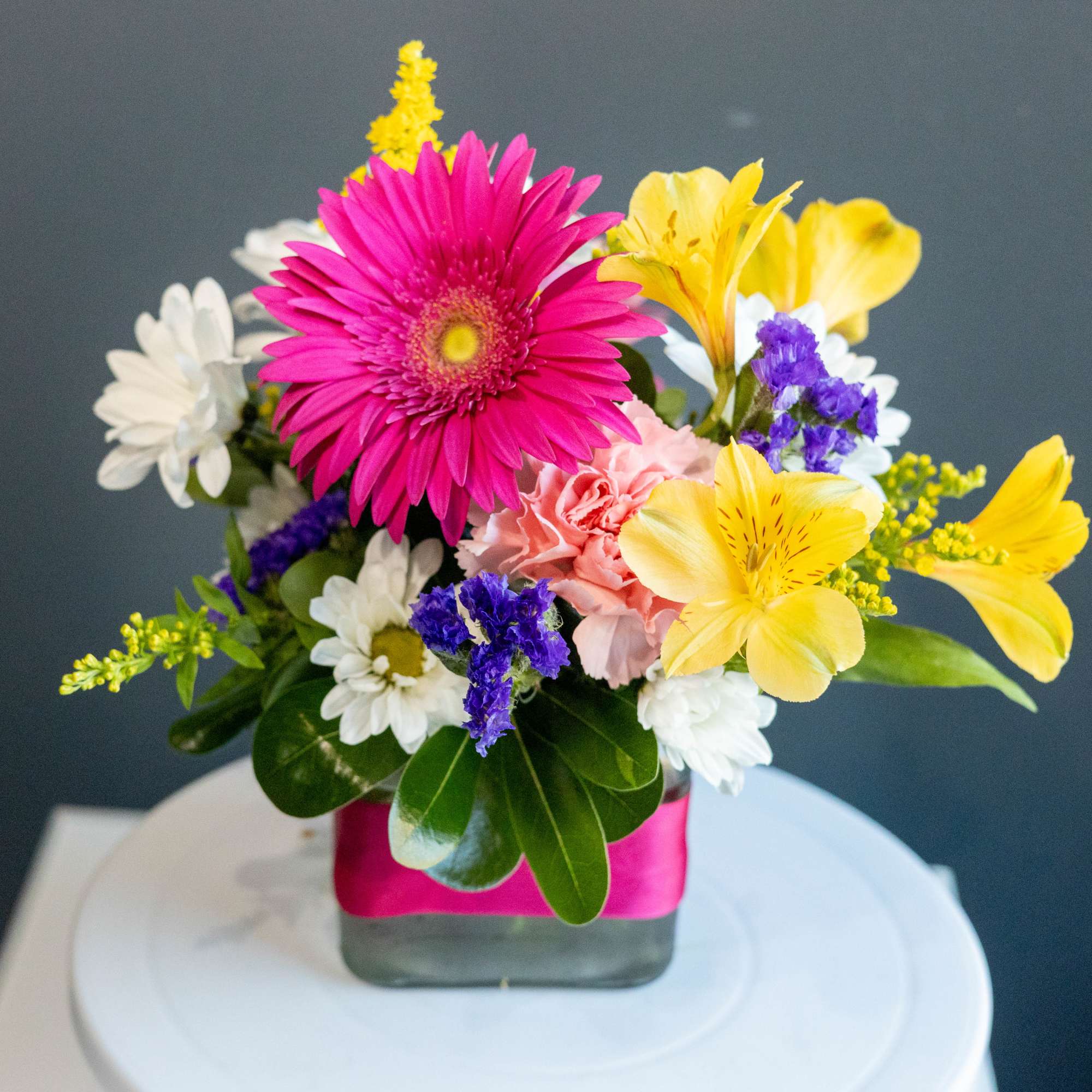 Colorful mixed bouquet in a square glass vase with a pink wrap