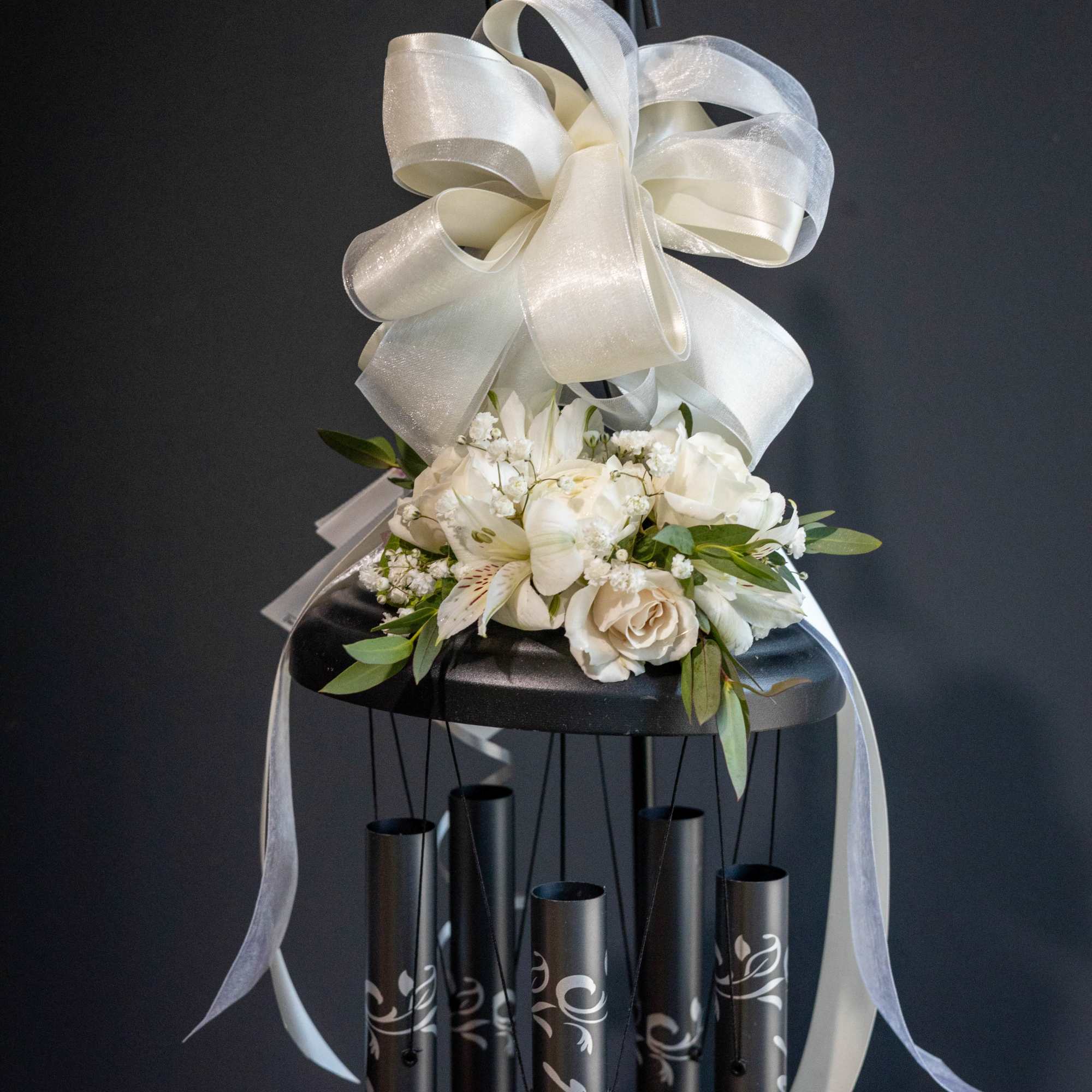 White floral arrangement with a large ivory bow on a black wind chime