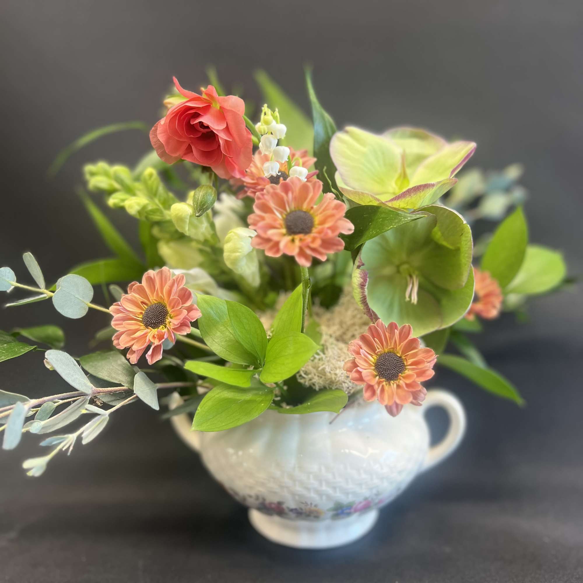 Mixed floral arrangement in a white handled vase with coral and green blooms