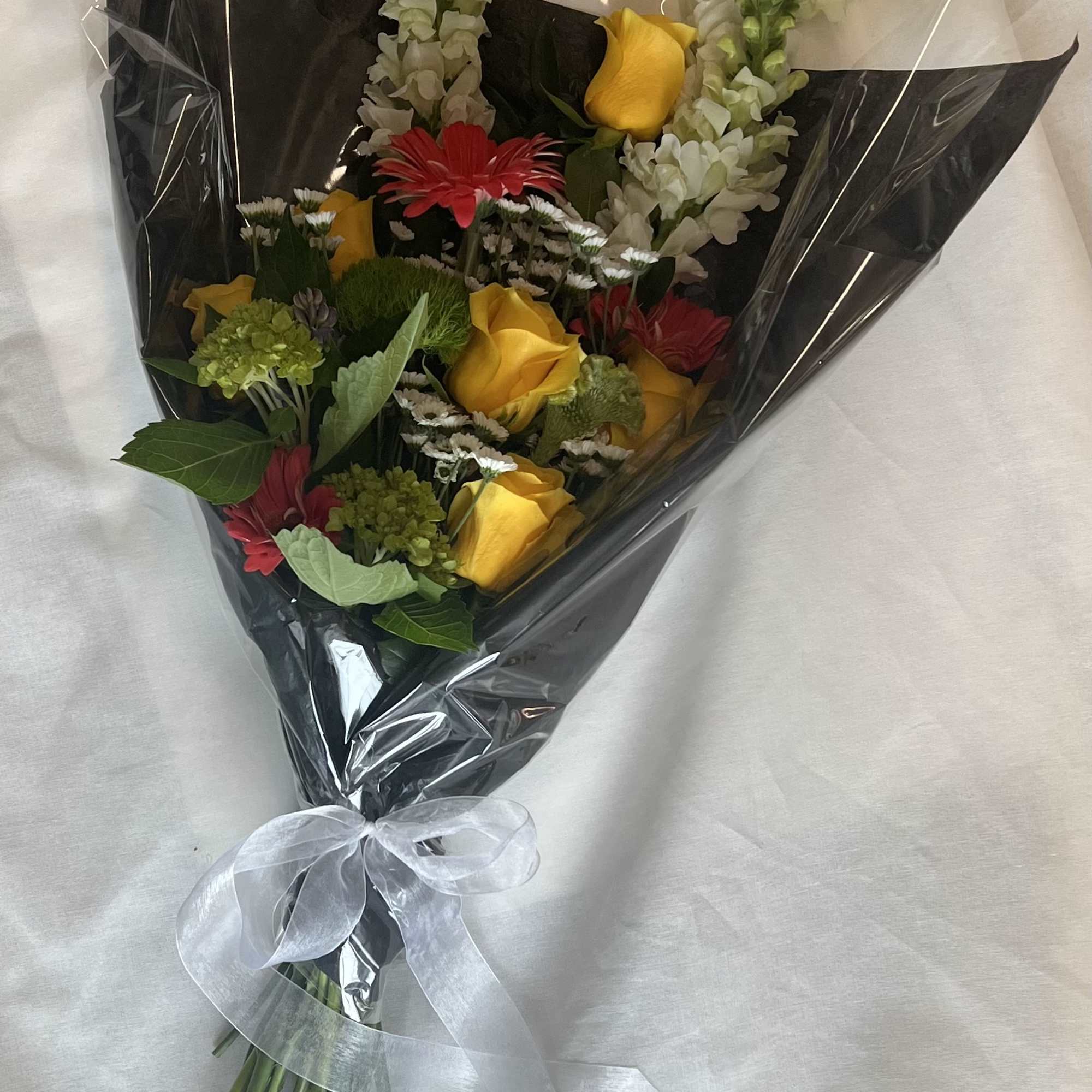 Bouquet of yellow roses, red gerberas, and white snapdragons wrapped in black paper