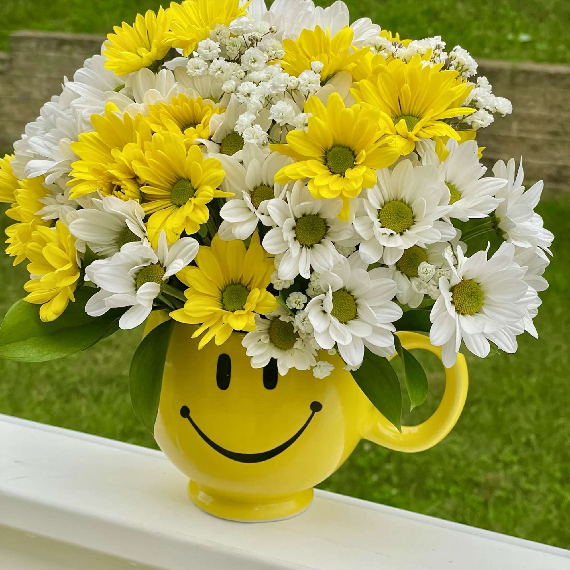 Yellow and white daisy bouquet in a smiley-face mug