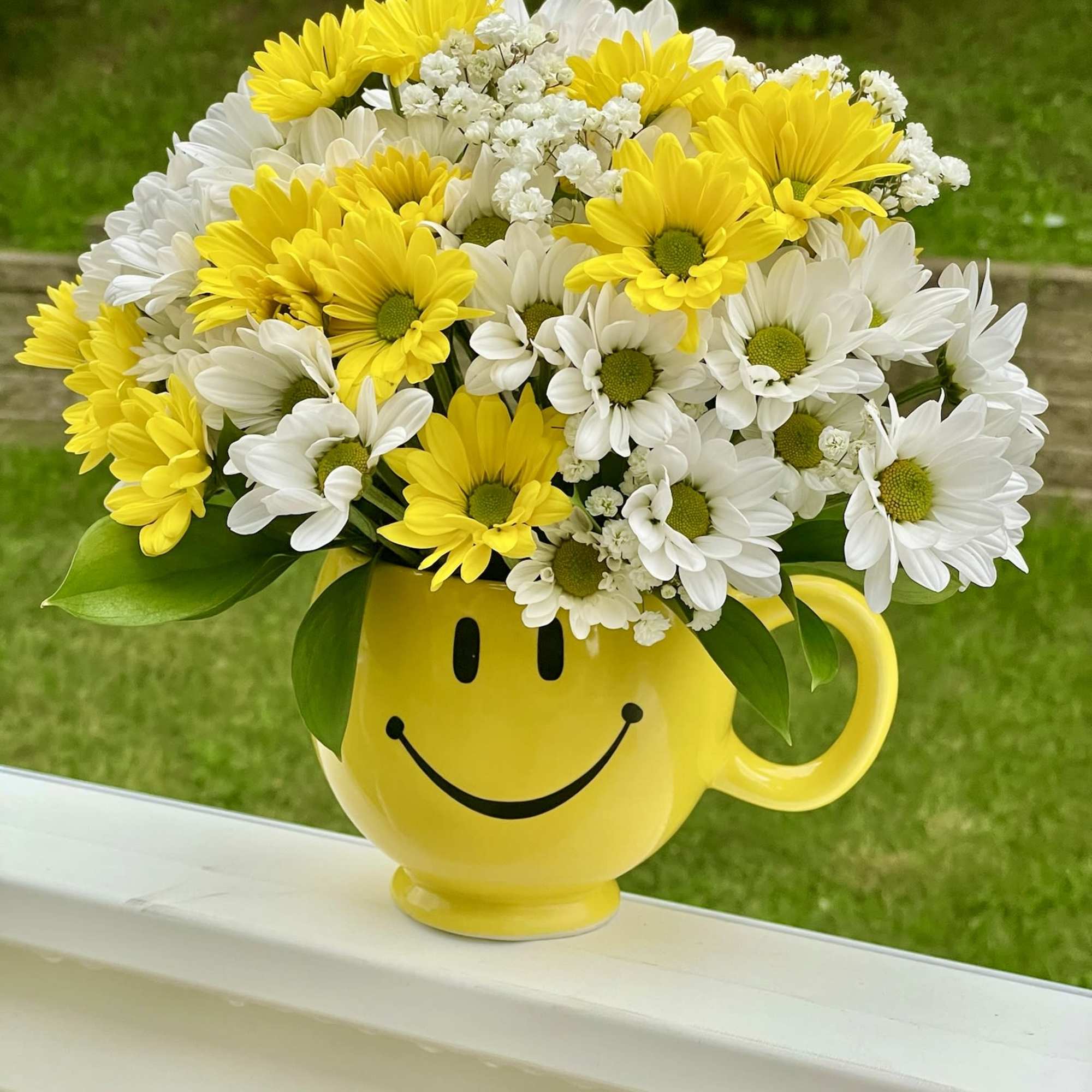 Yellow and white daisy bouquet in a smiley-face mug