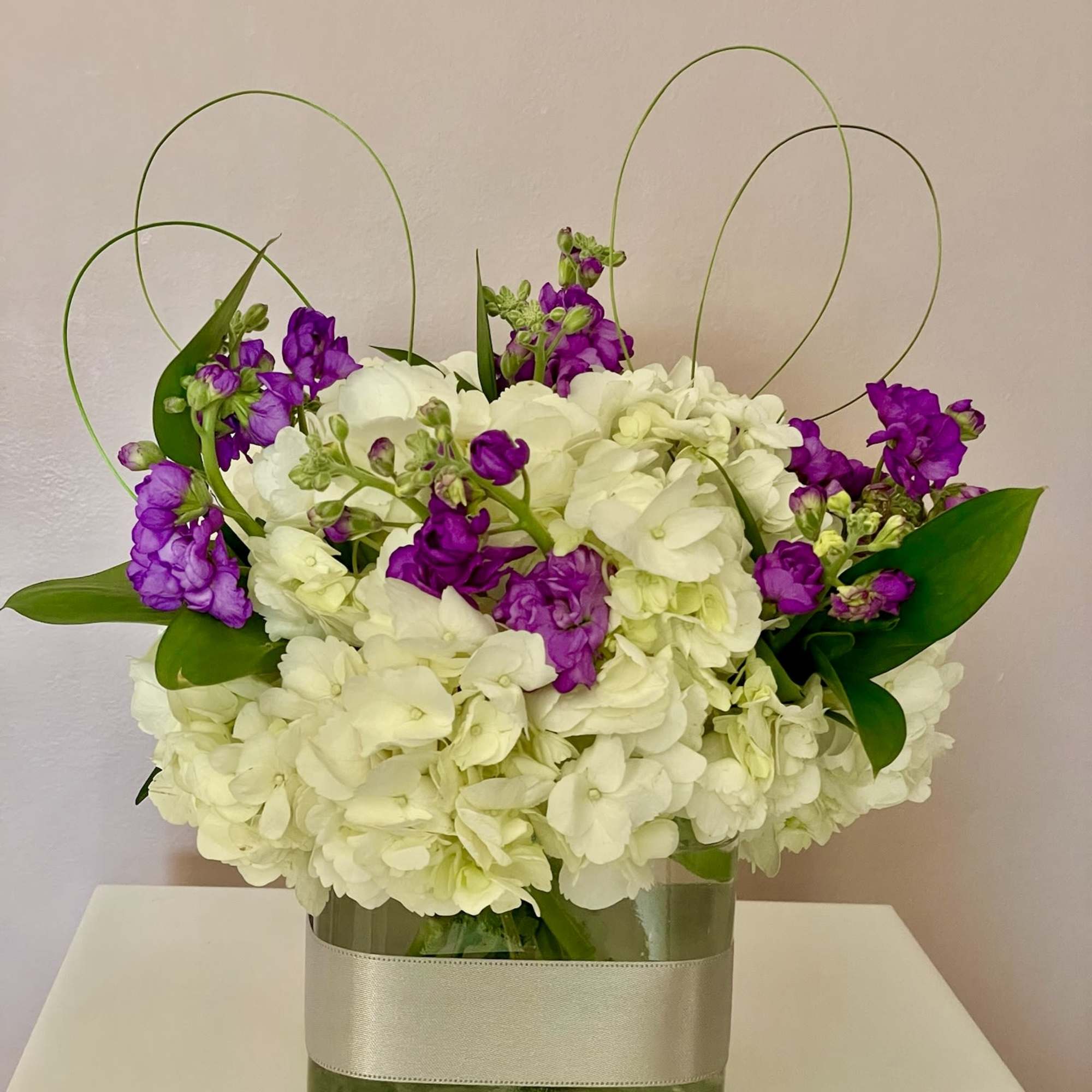 White hydrangea and purple flowers in a square glass vase