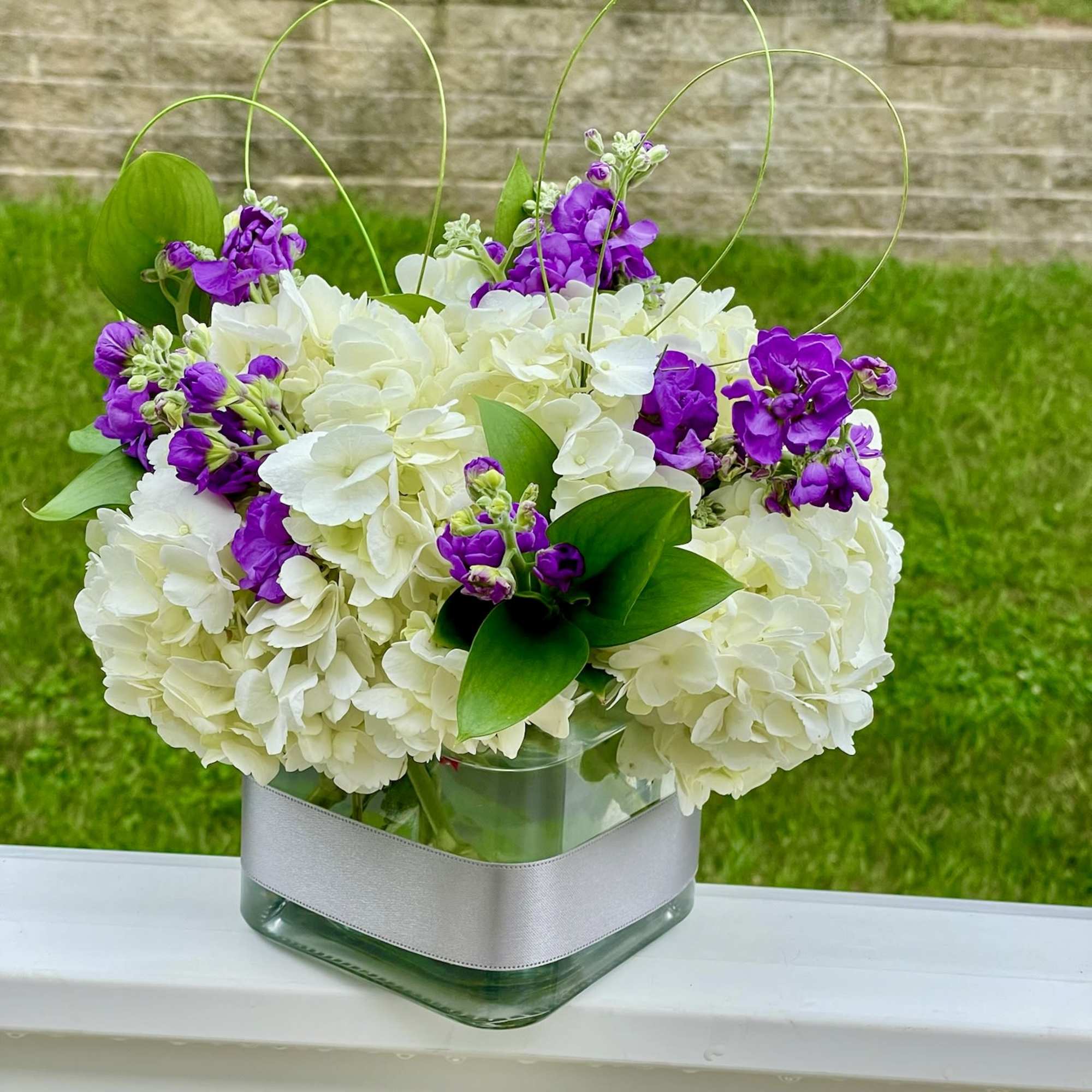 White hydrangeas and purple flowers in a square glass vase
