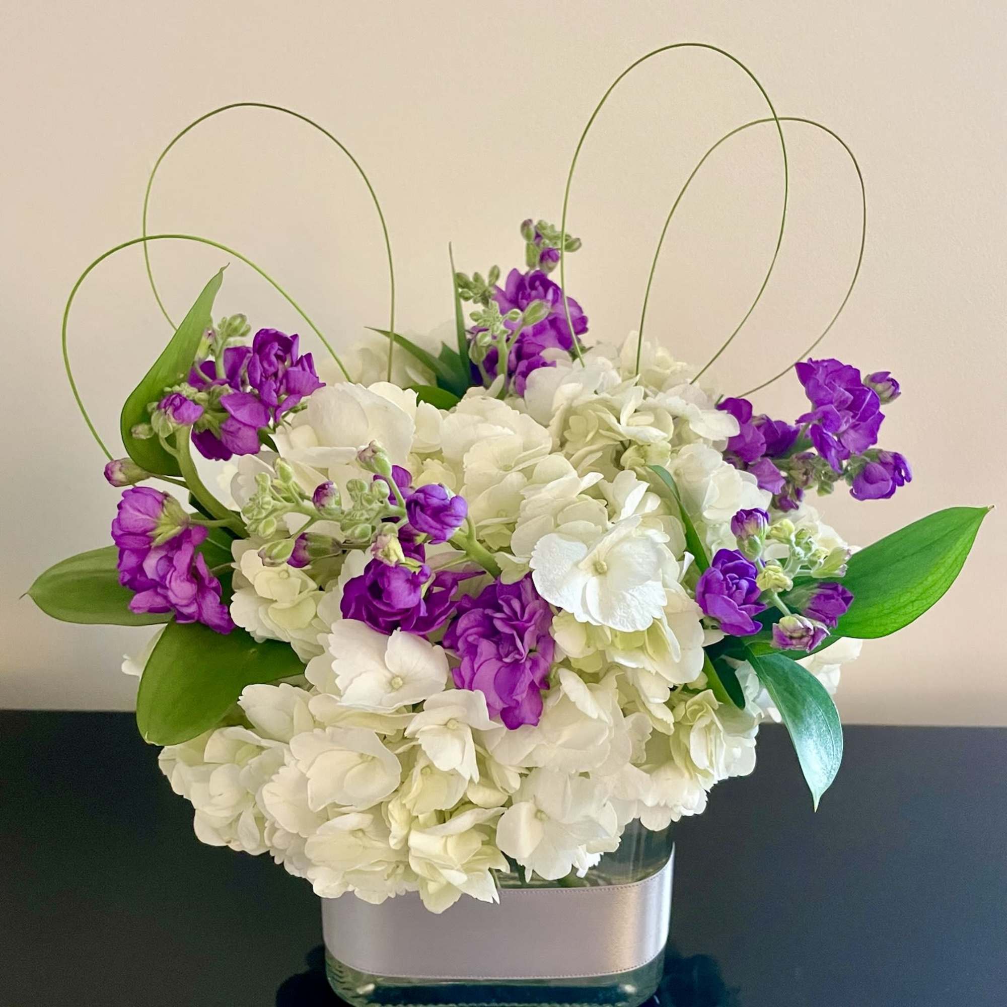 White hydrangea and purple flowers in a glass vase with looped grass