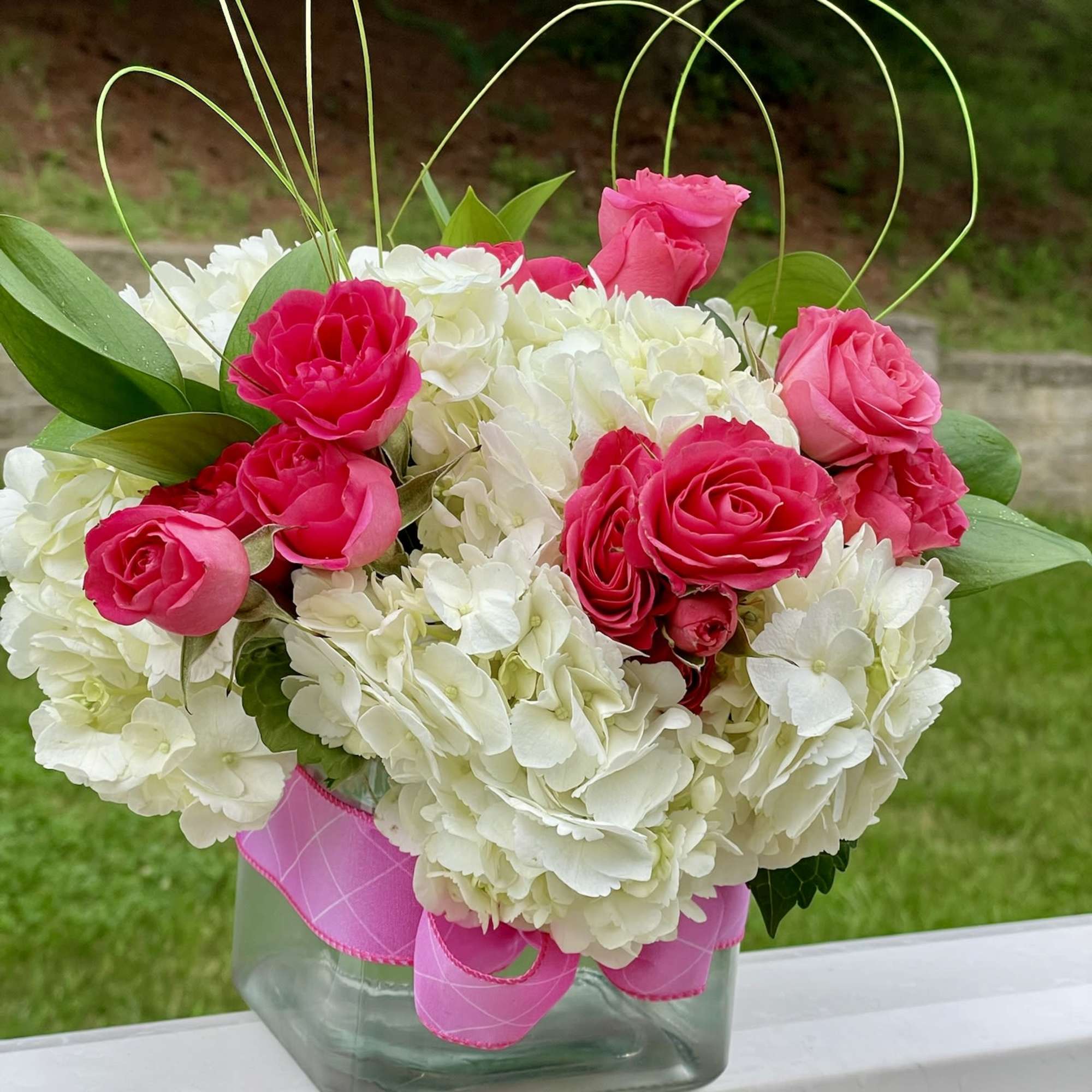 Pink roses and white hydrangeas in a glass vase with ribbon