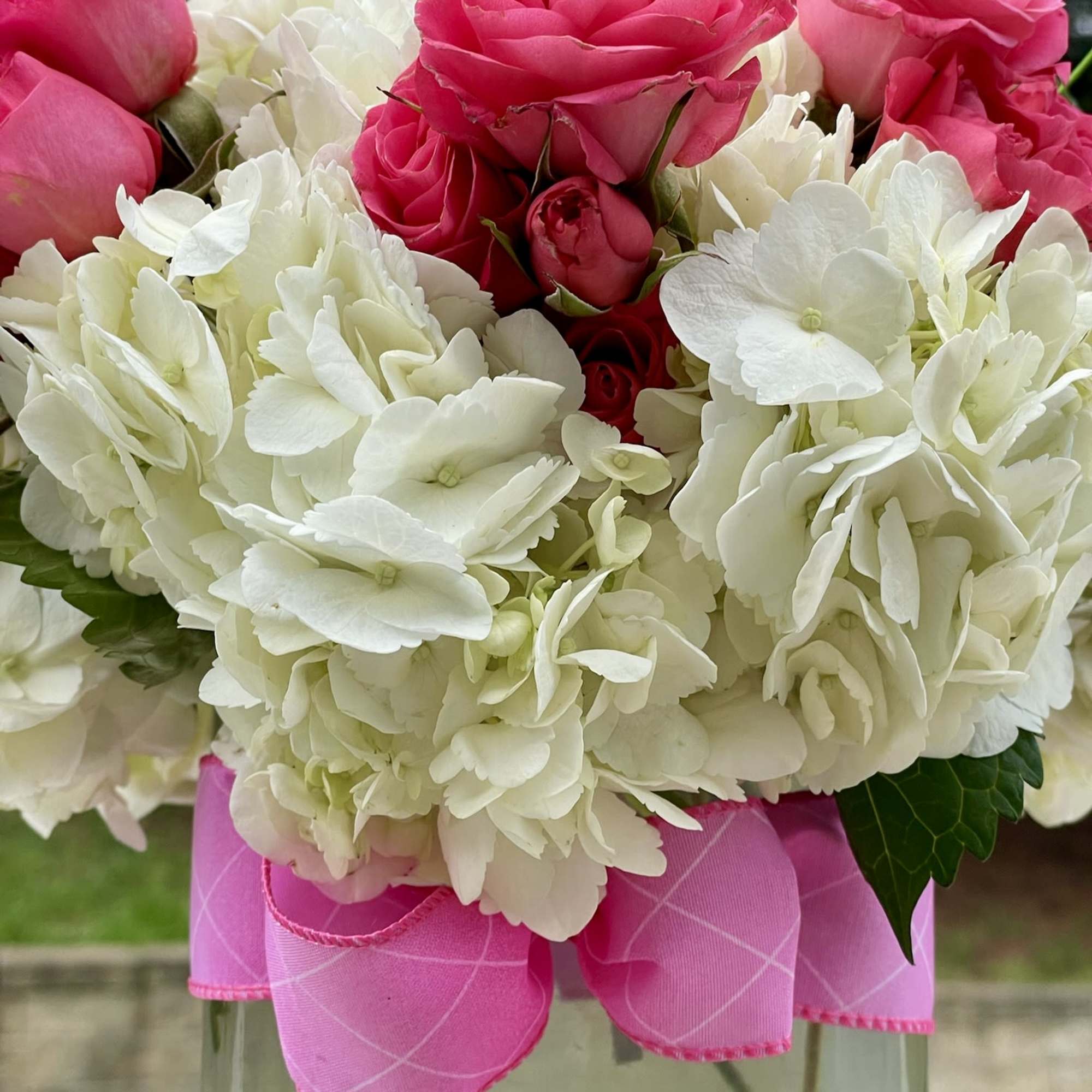 Pink roses and white hydrangeas in a clear glass vase with a pink ribbon