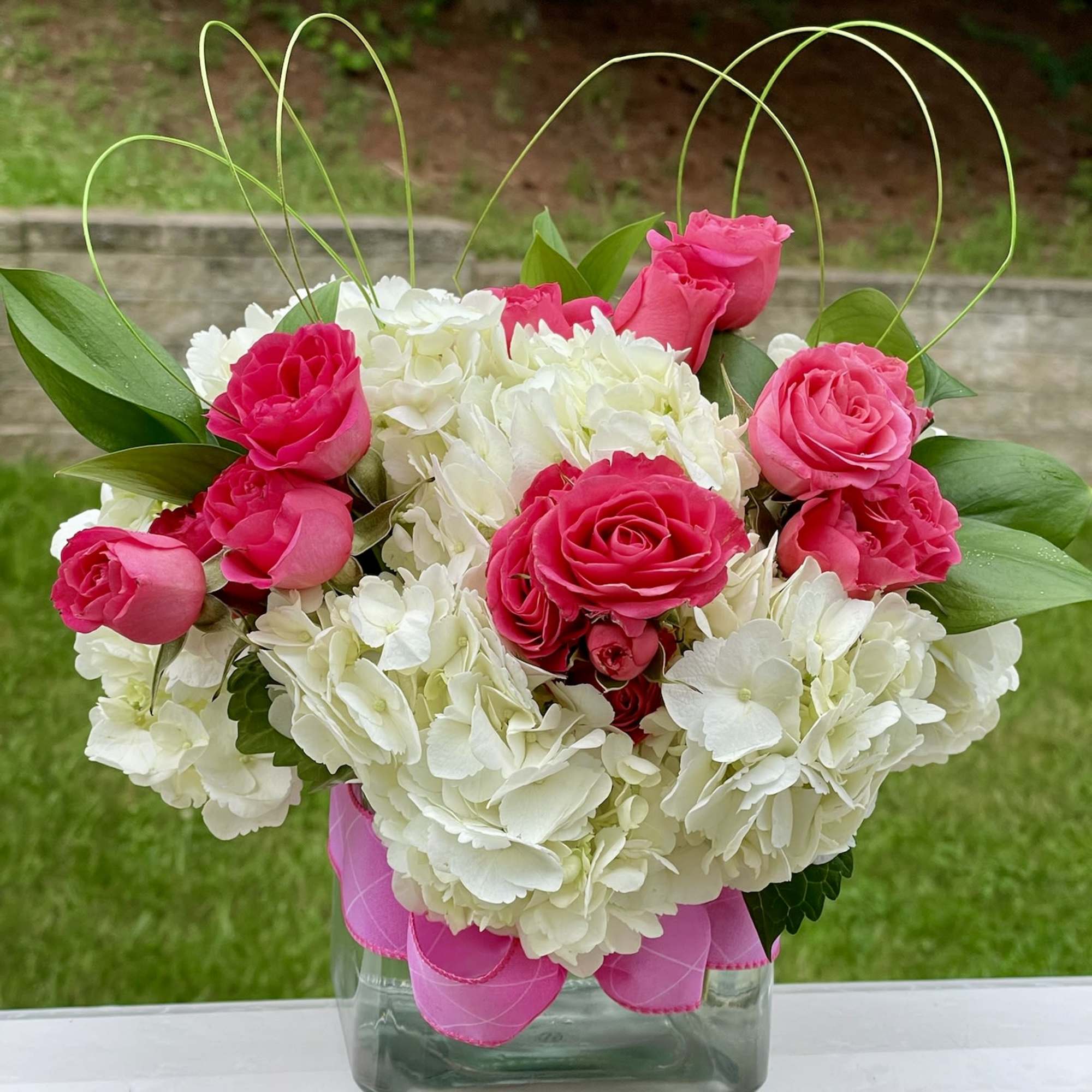 Pink roses and white hydrangeas in a square glass vase with ribbon