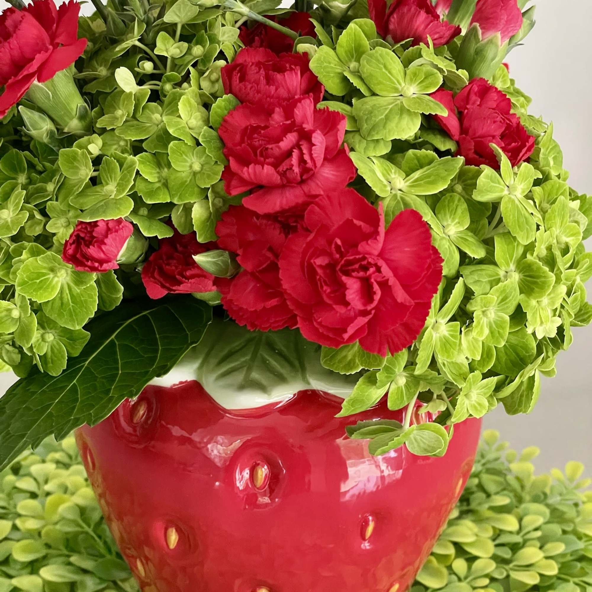 Red carnations in a red strawberry-shaped pot with bright green filler