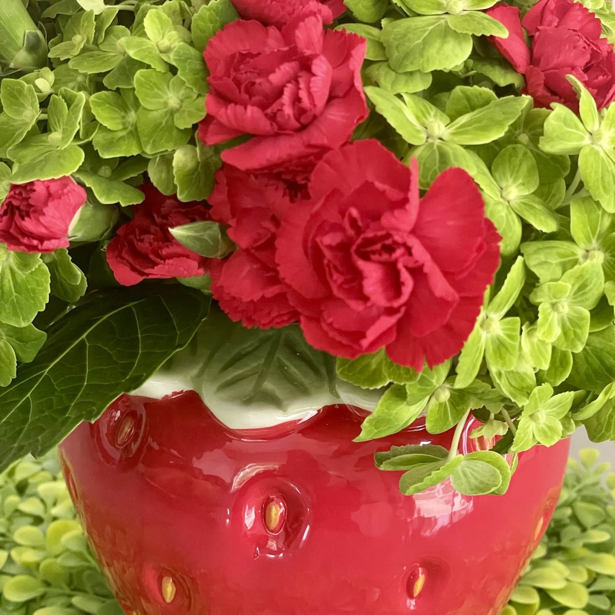 Red carnations in a glossy strawberry-shaped vase with bright green filler