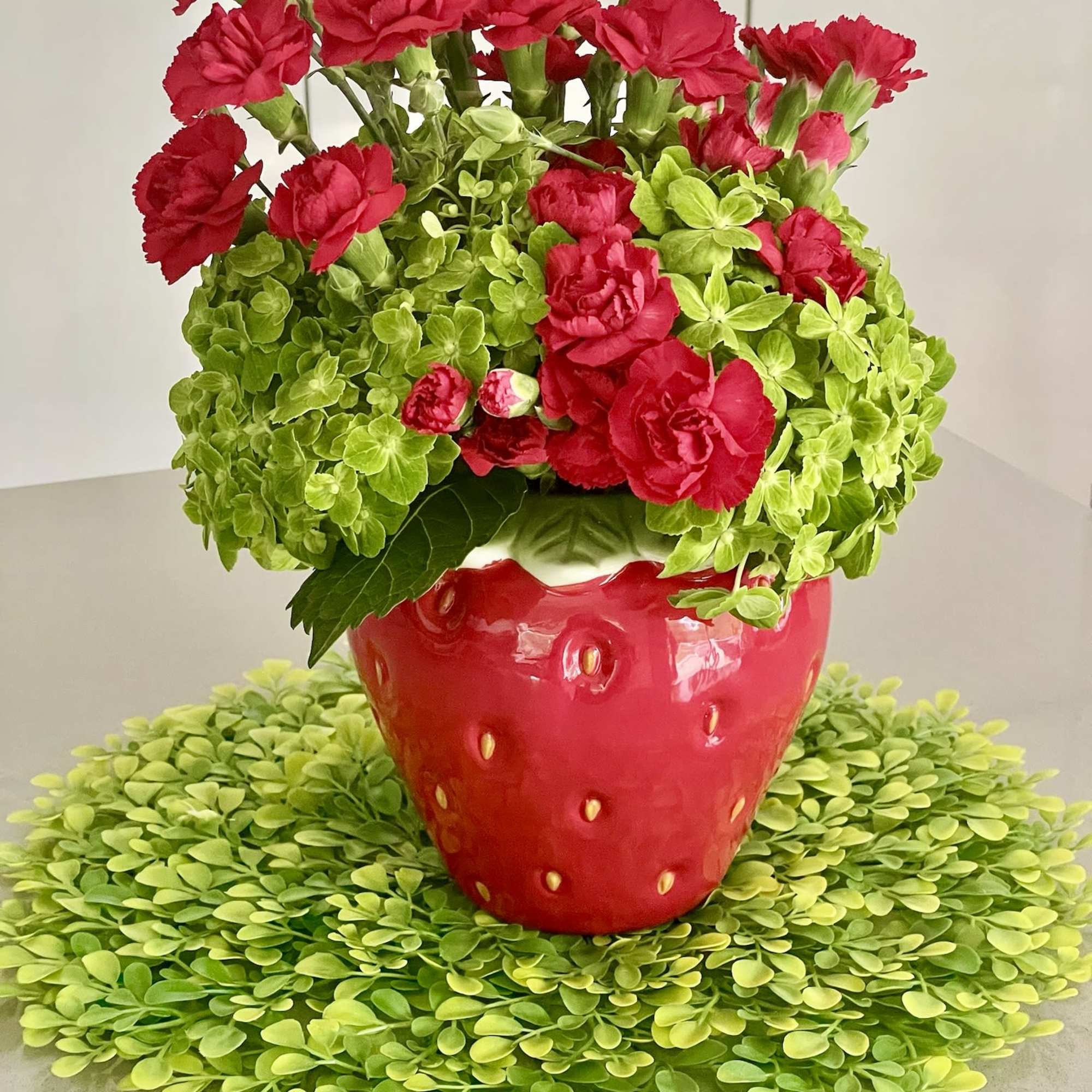 Red carnations in a strawberry-shaped red vase on a green placemat