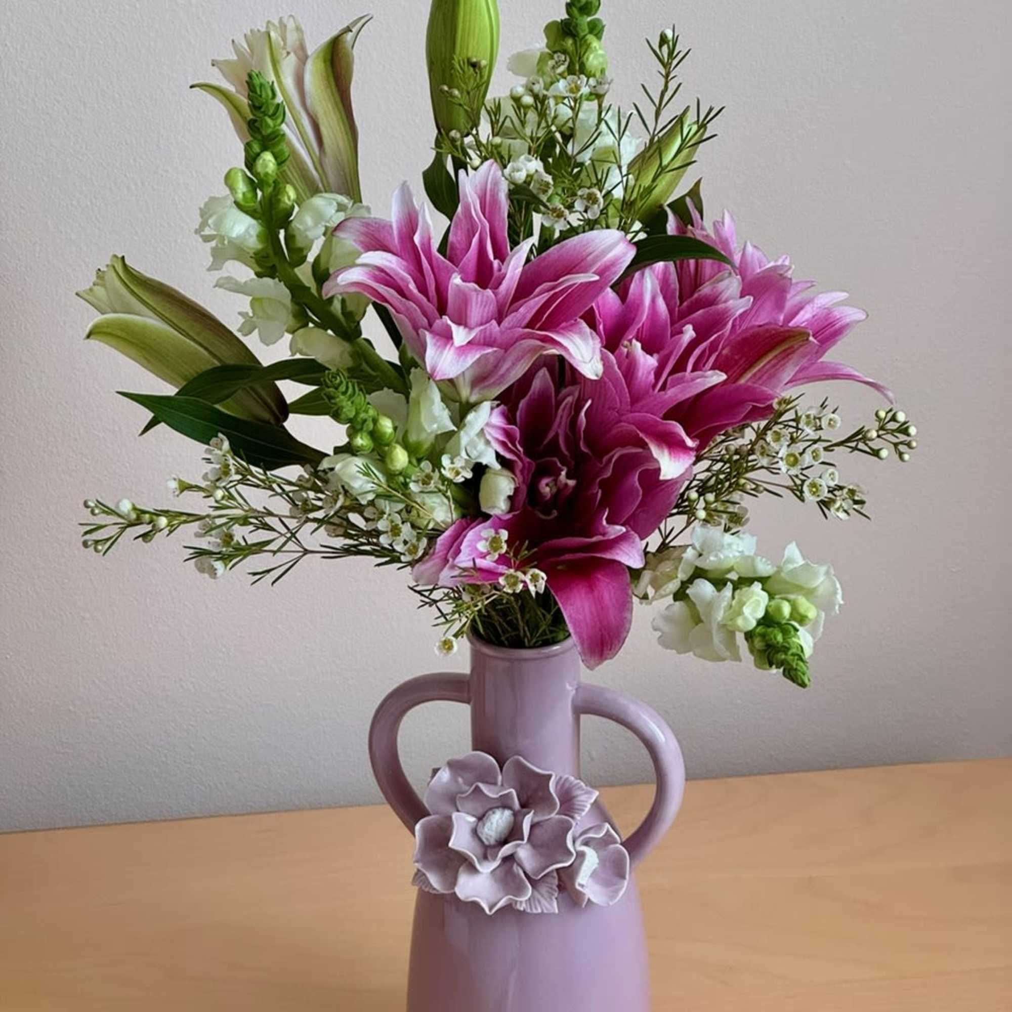 Pink lilies arranged in a lavender vase with white accent flowers