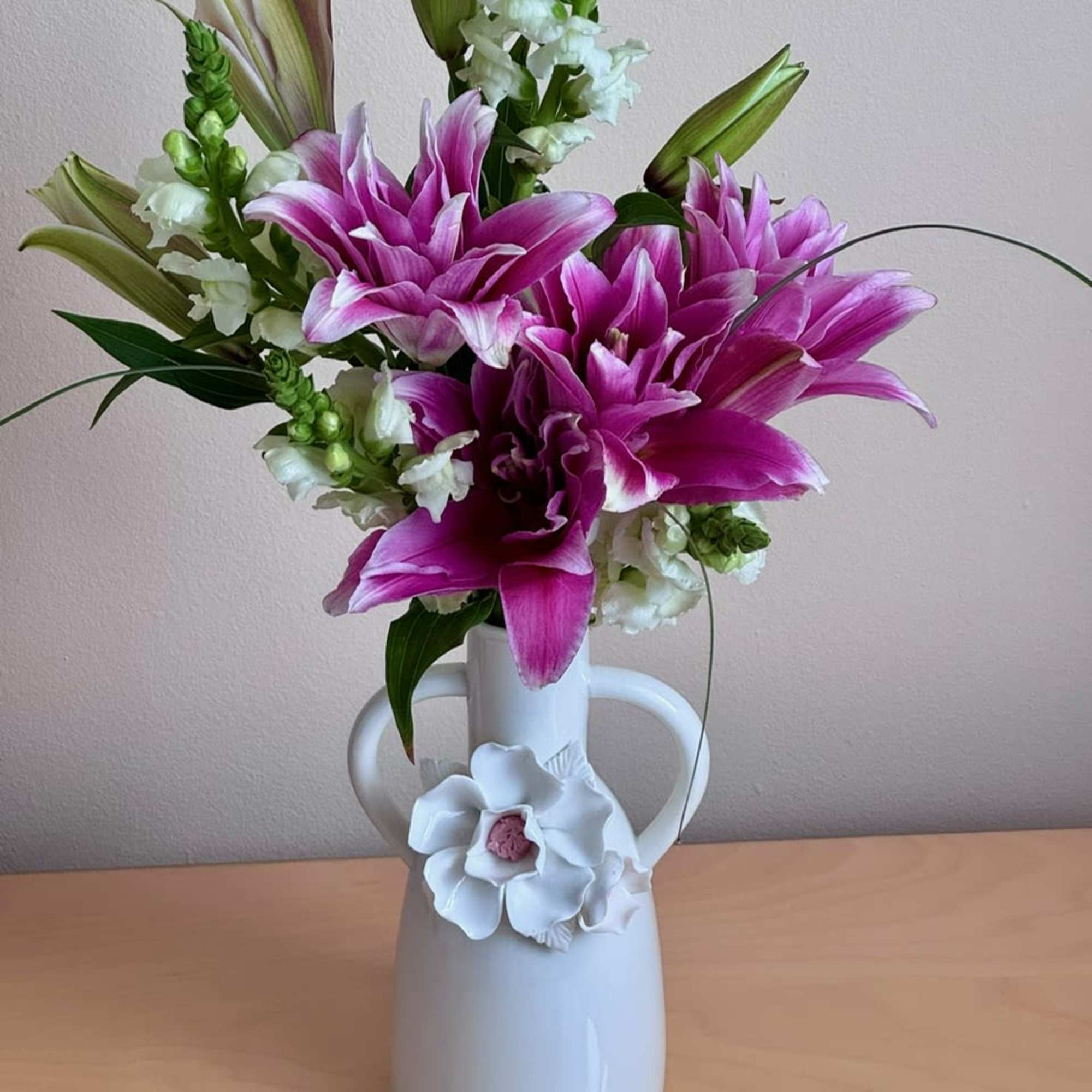 Pink lilies arranged in a white vase with white accent flowers