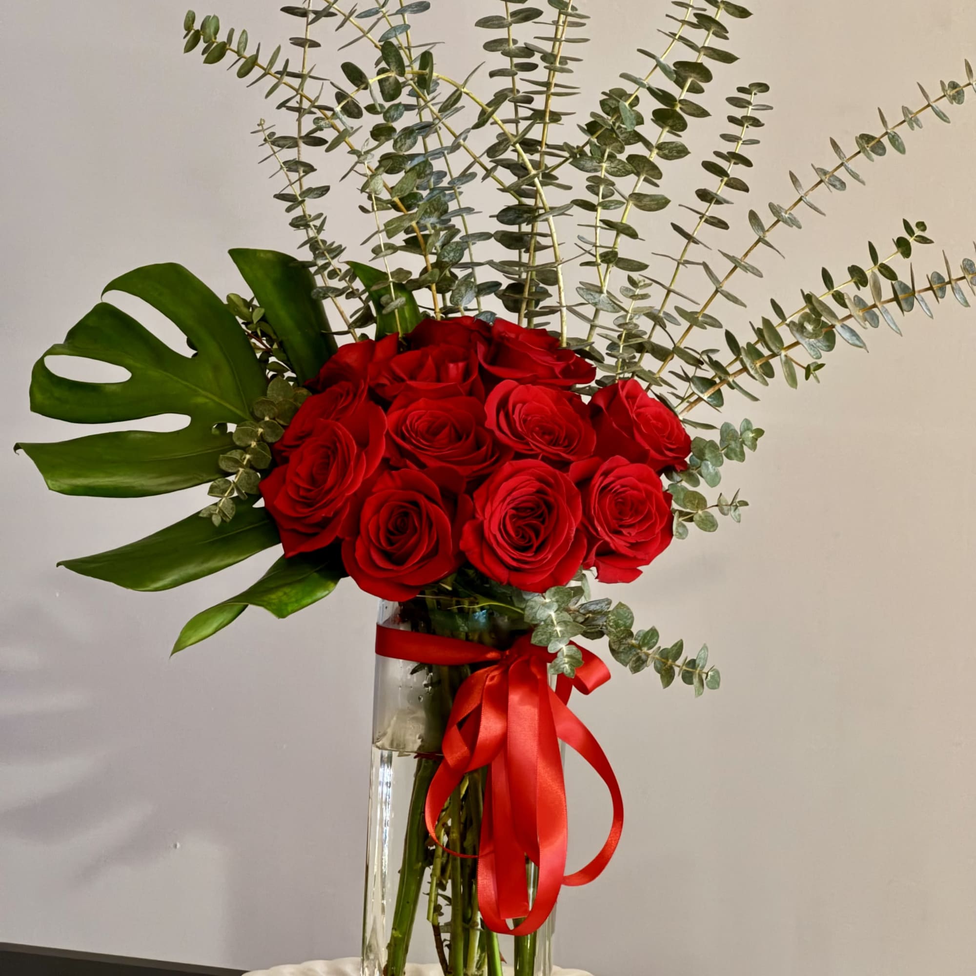 Red roses in a tall glass vase with a red ribbon