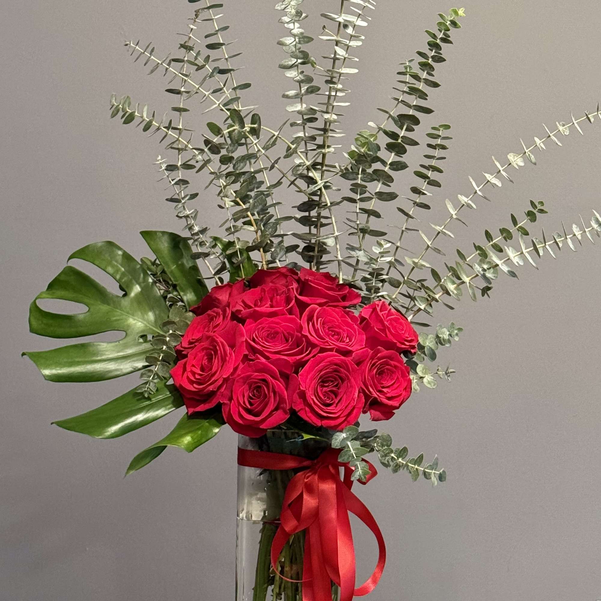 Red roses in a tall glass vase with eucalyptus and a red ribbon