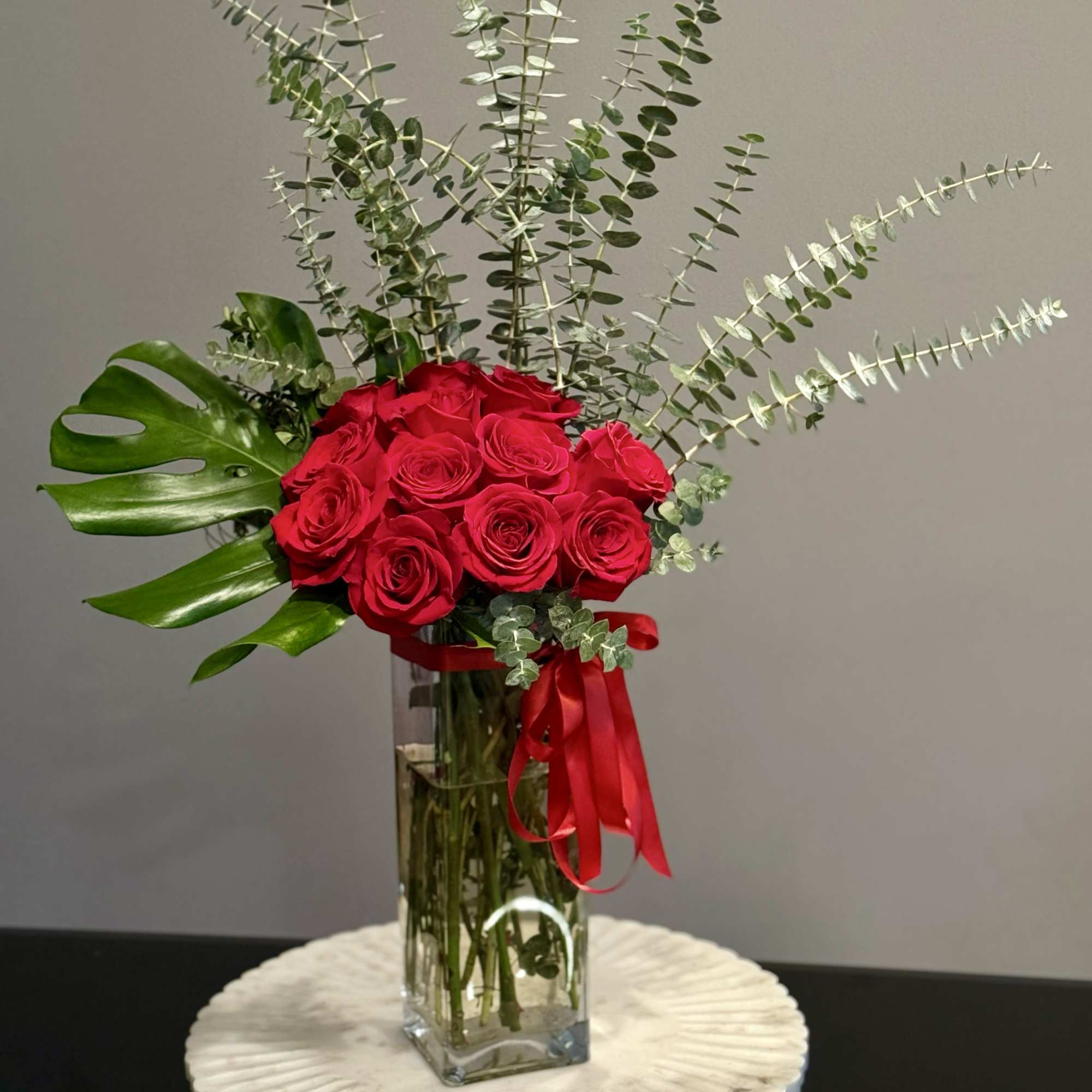 Red roses in a clear rectangular vase with eucalyptus and a red ribbon