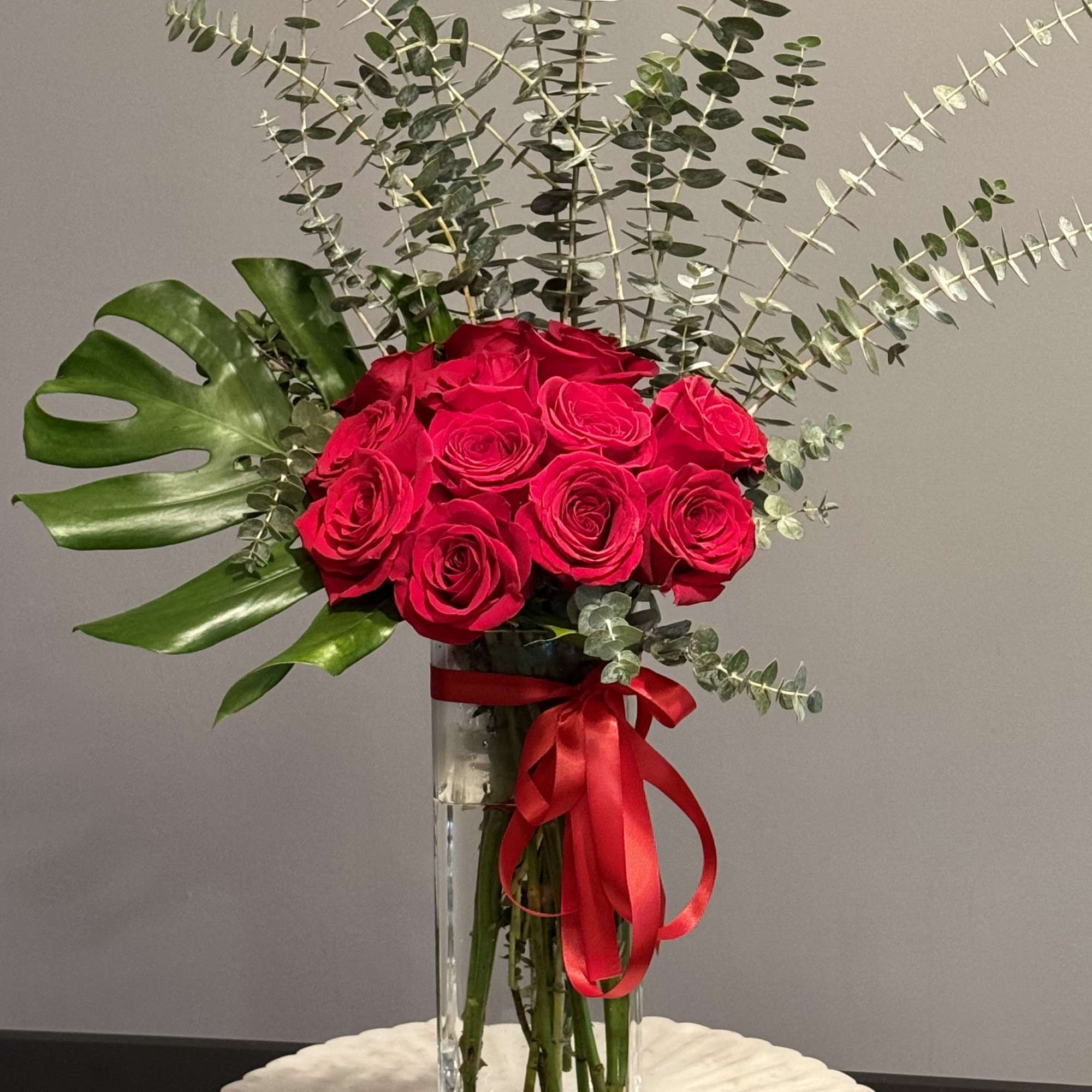 Red roses in a tall glass vase with eucalyptus and a red ribbon, photo 3 of 3