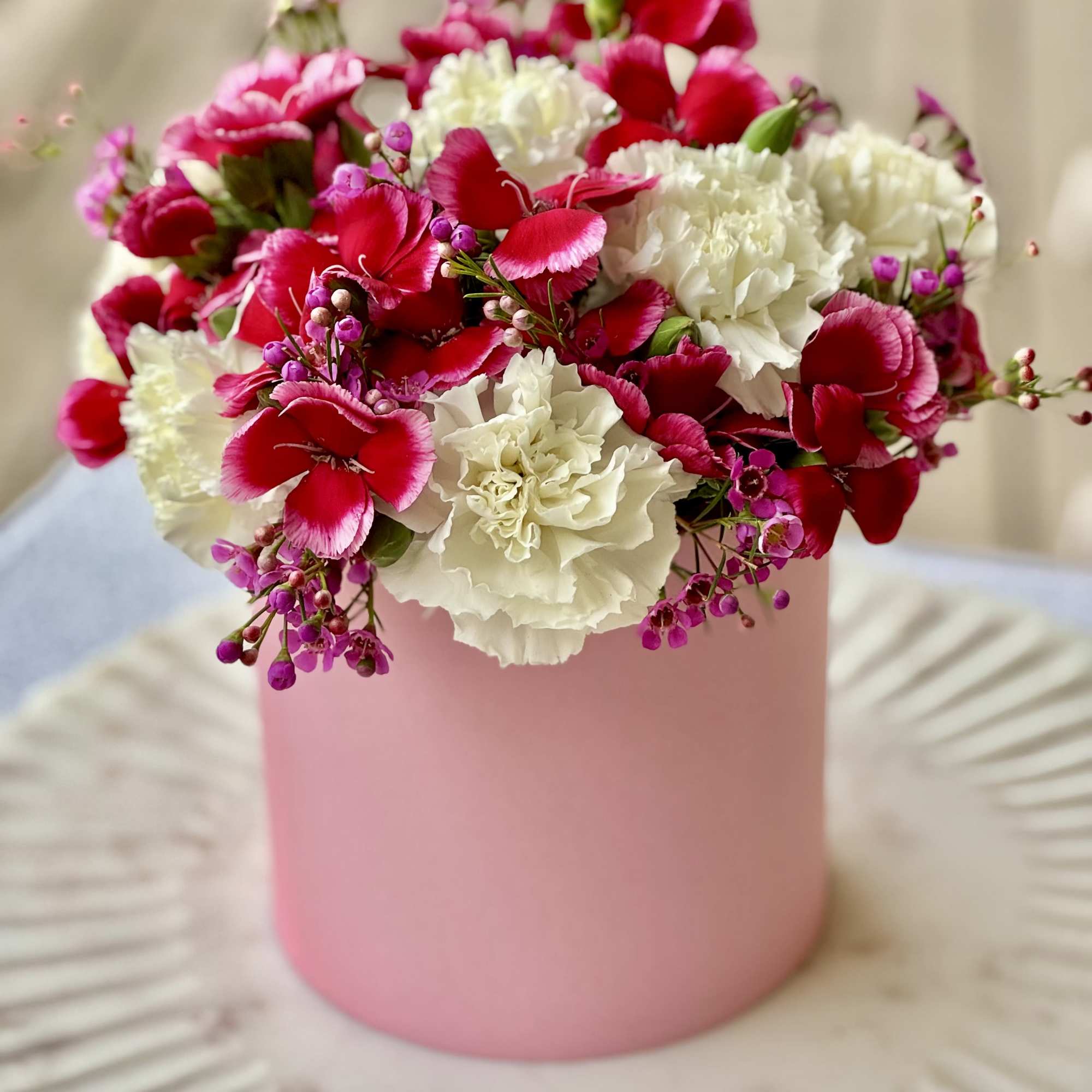 Pink and white carnations arranged in a pink cylindrical box
