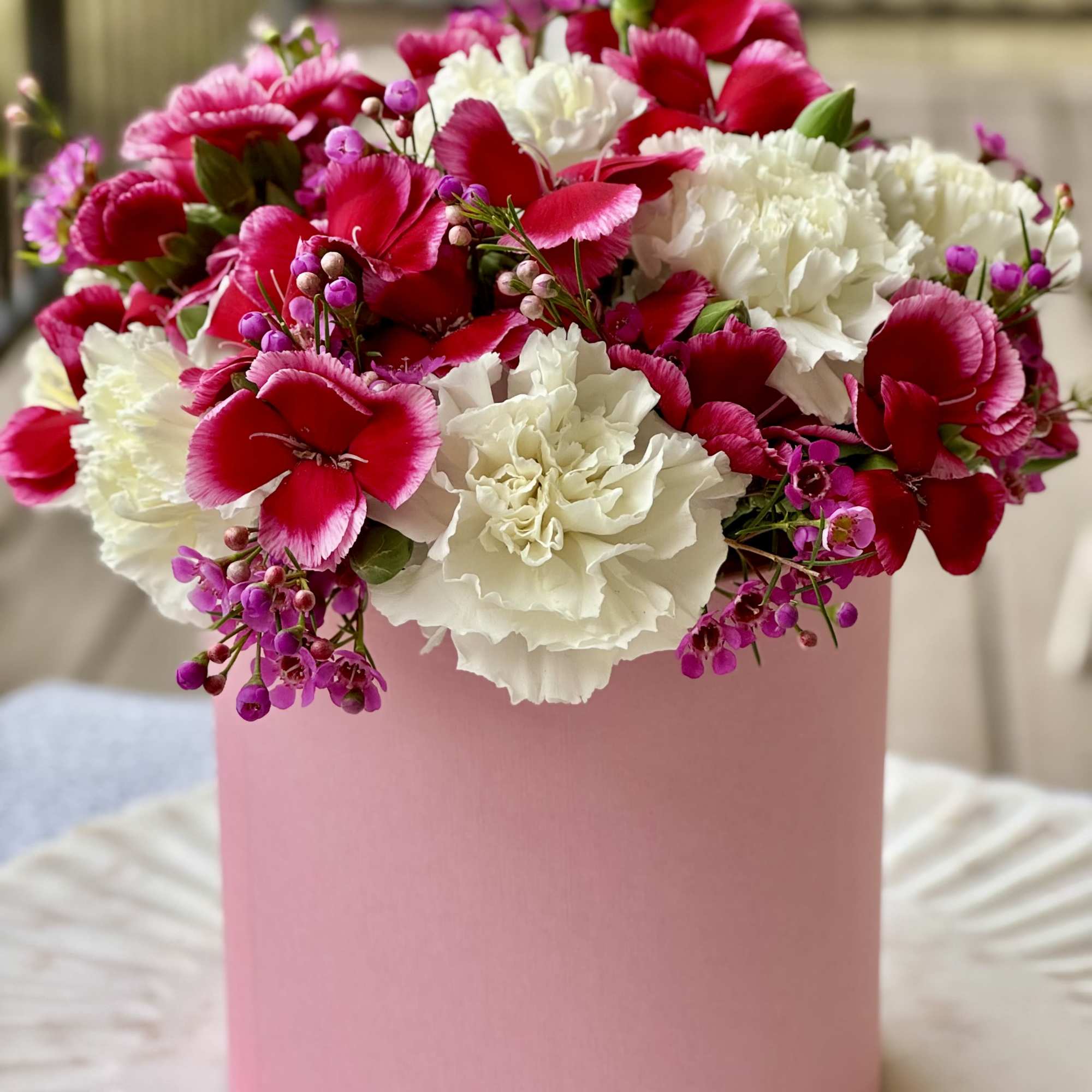 Pink and white carnations with small purple flowers in a pink box