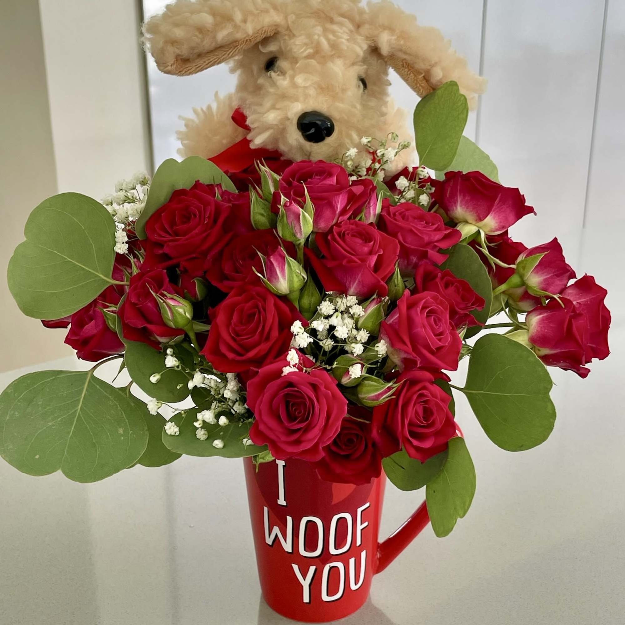 Red roses in a mug with a plush dog peeking over the top