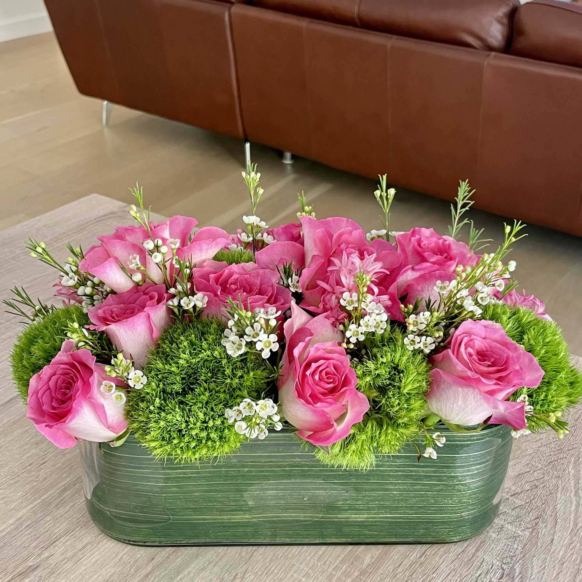 Pink roses arranged in a green rectangular container with white filler flowers