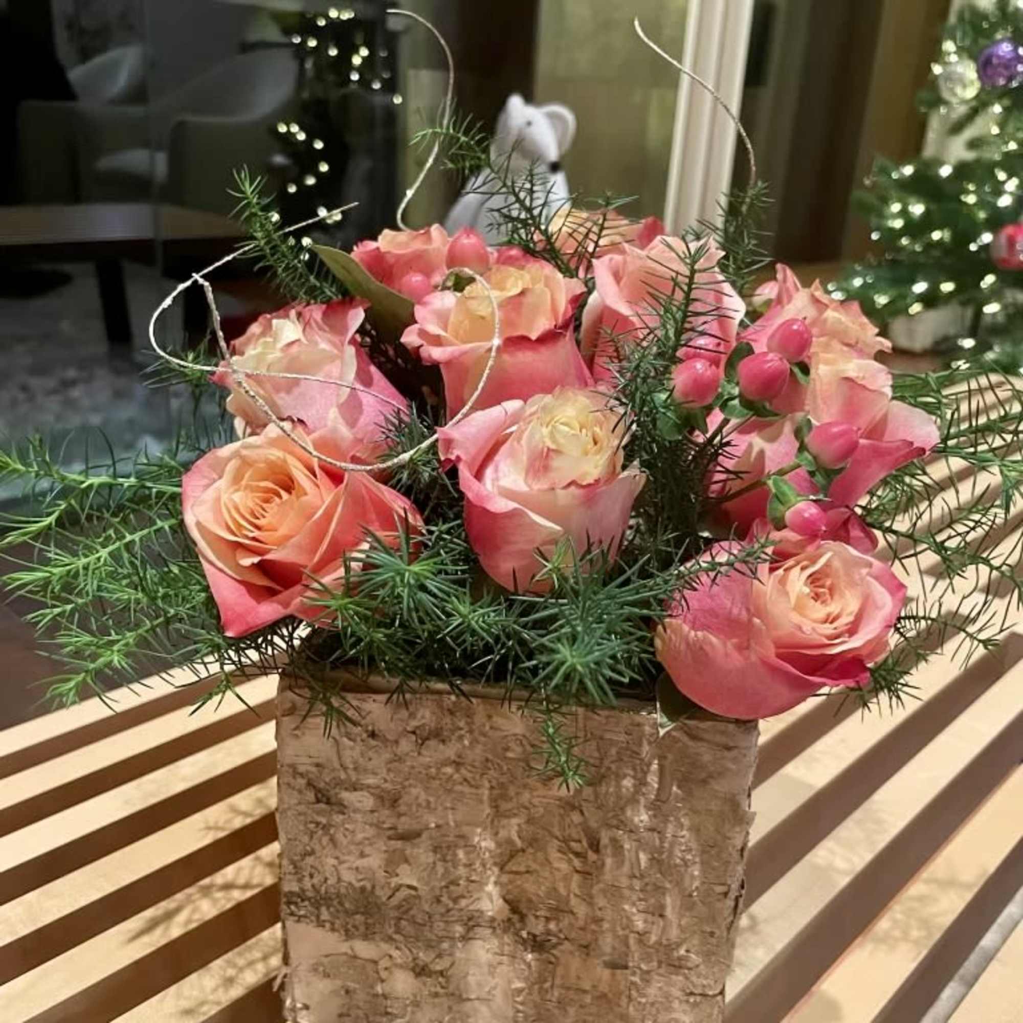 Pink and peach roses in a birch bark container with airy greenery