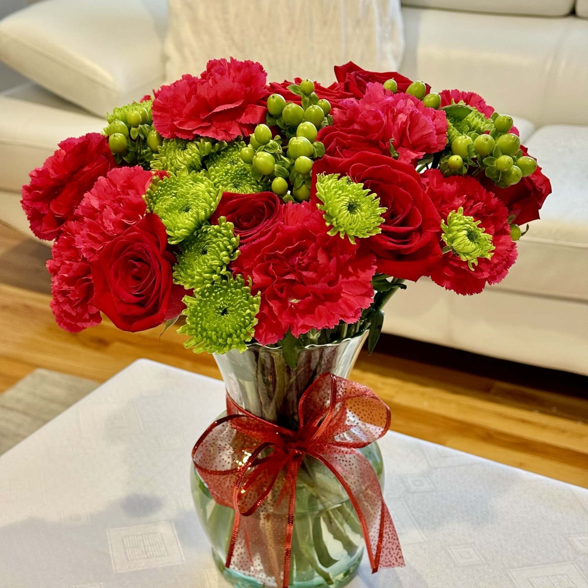 Red roses and pink carnations in a glass vase with a red ribbon