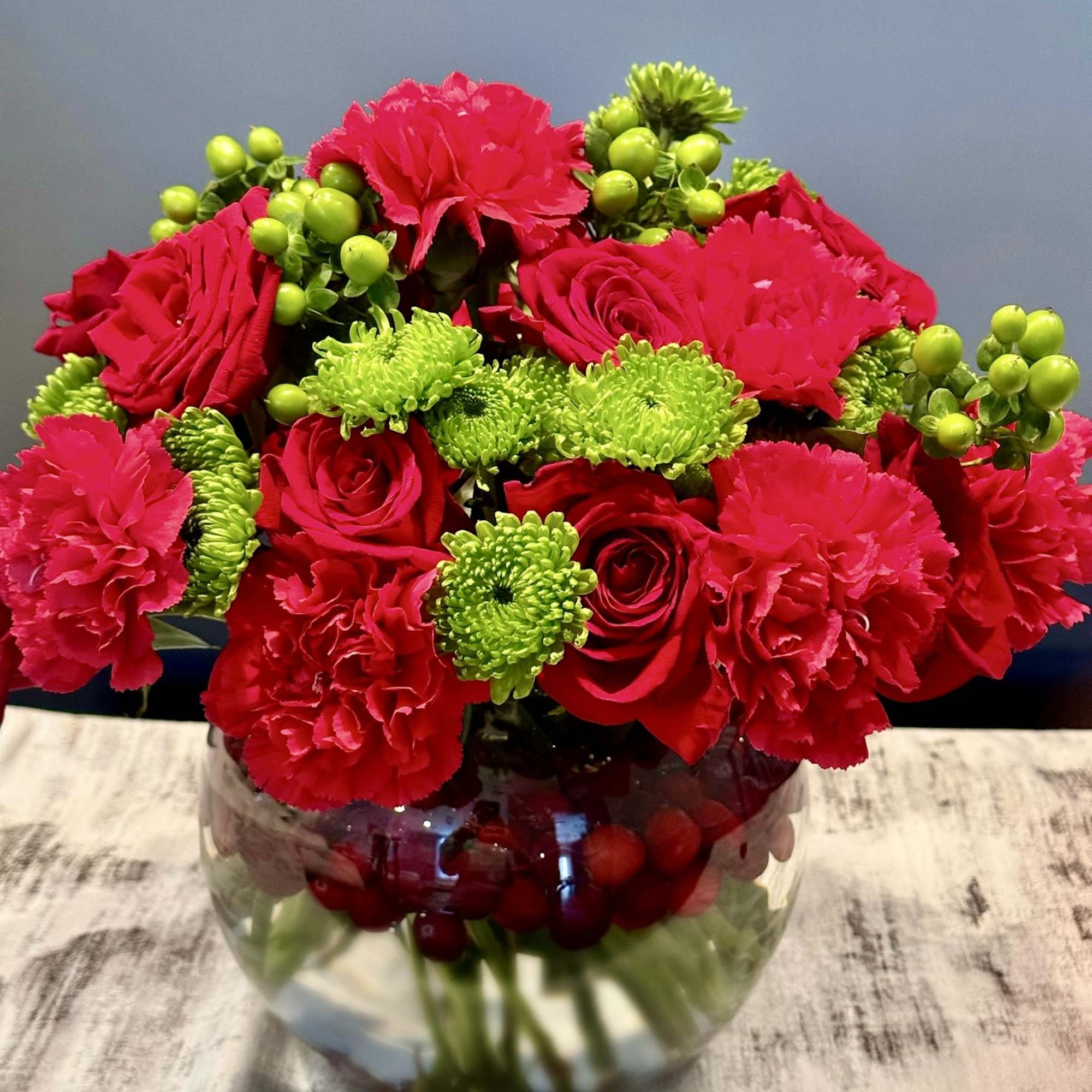 Red roses and carnations in a glass vase with green button mums