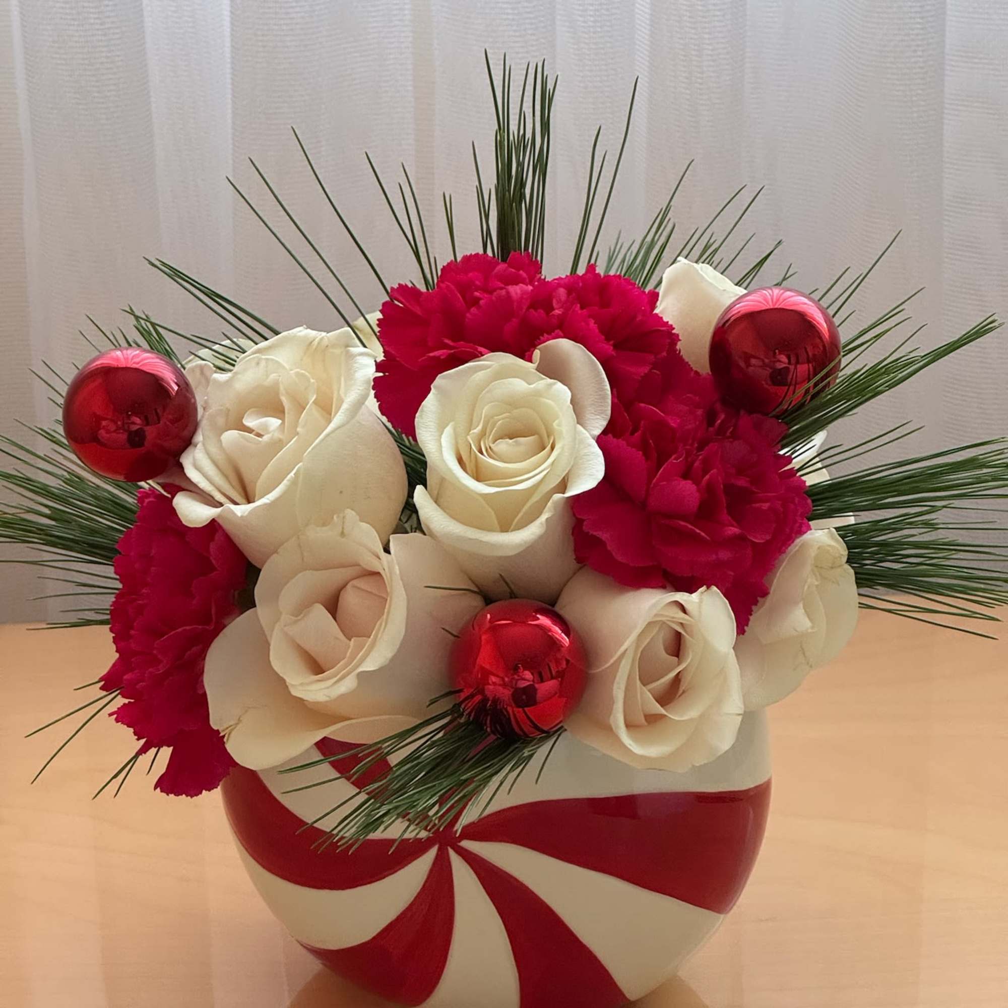 White roses and red carnations in a candy cane vase with red ornaments
