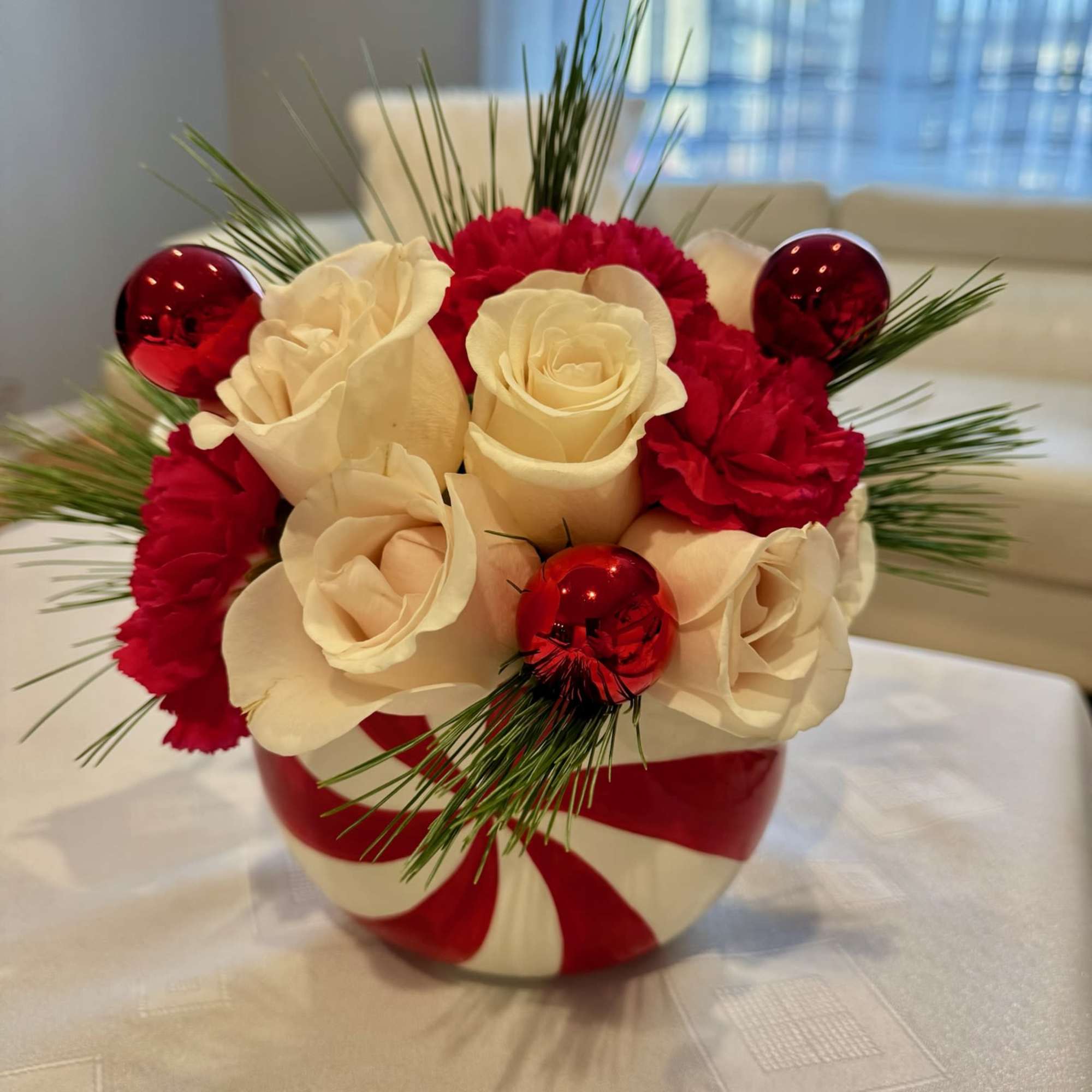Red and white rose arrangement in a striped round vase with pine accents
