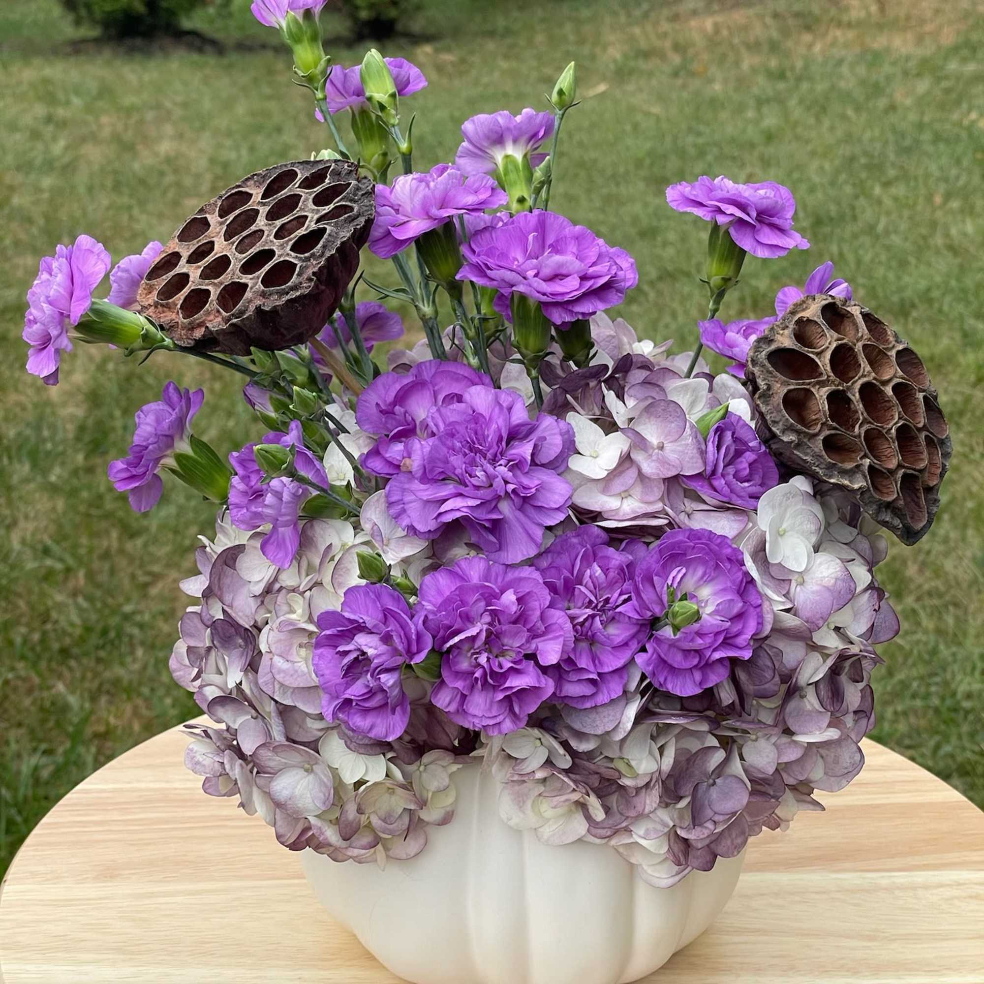 Purple flowers and hydrangeas arranged in a white pumpkin-shaped vase