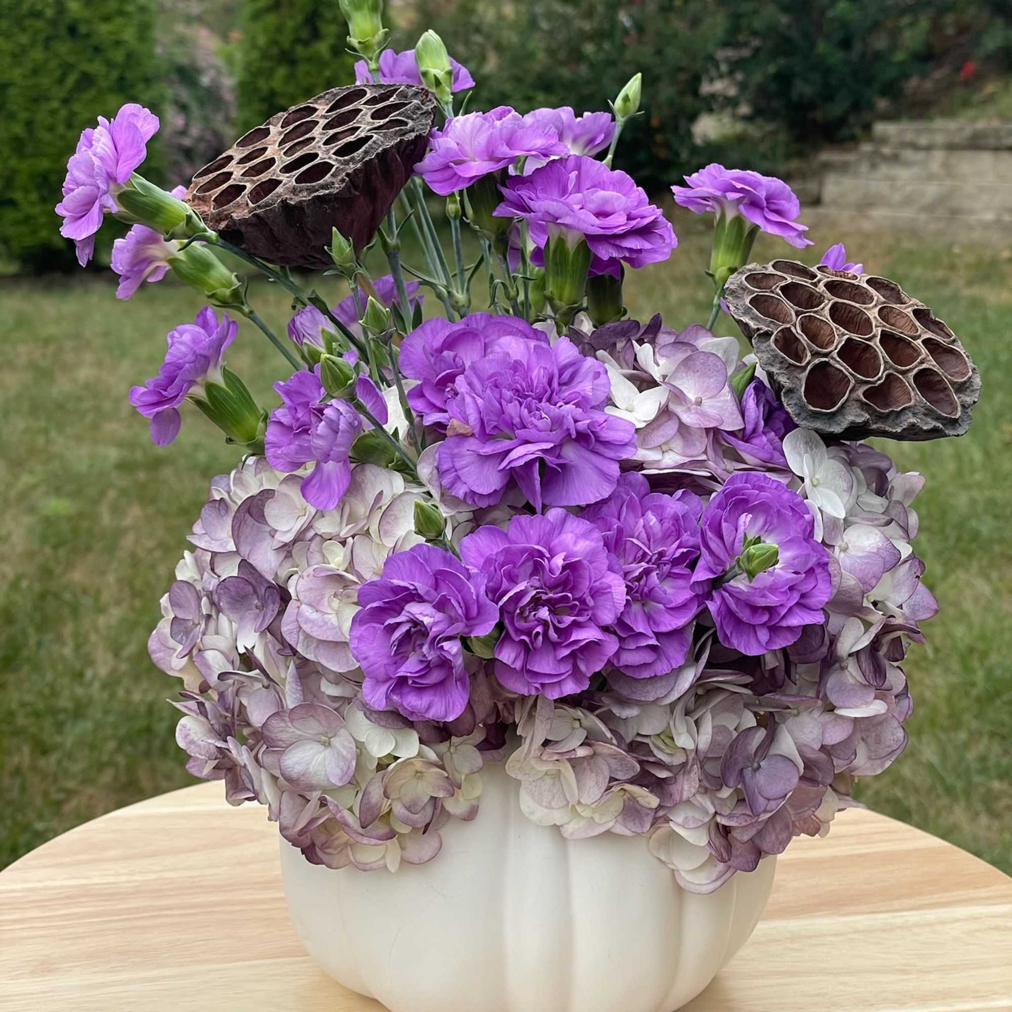 Purple carnations and hydrangeas in a white pumpkin vase