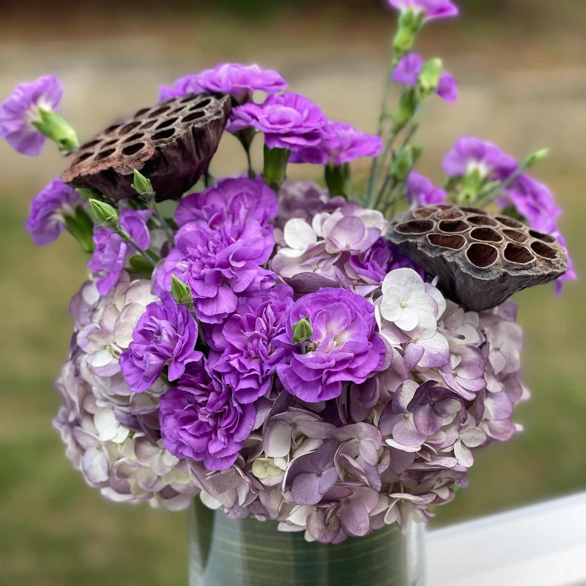 Purple hydrangea and carnations in a glass vase with lotus pods