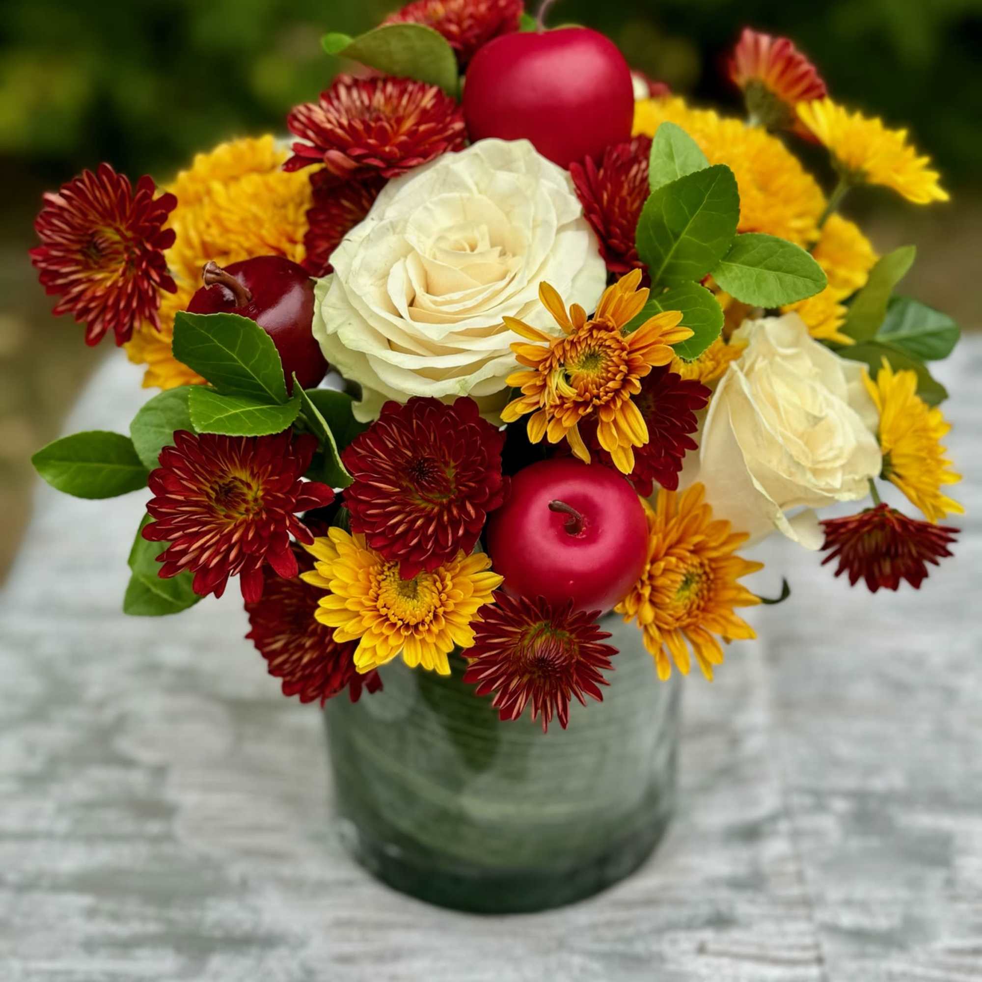Bouquet of white roses, red and yellow mums, and red apples in a green vase