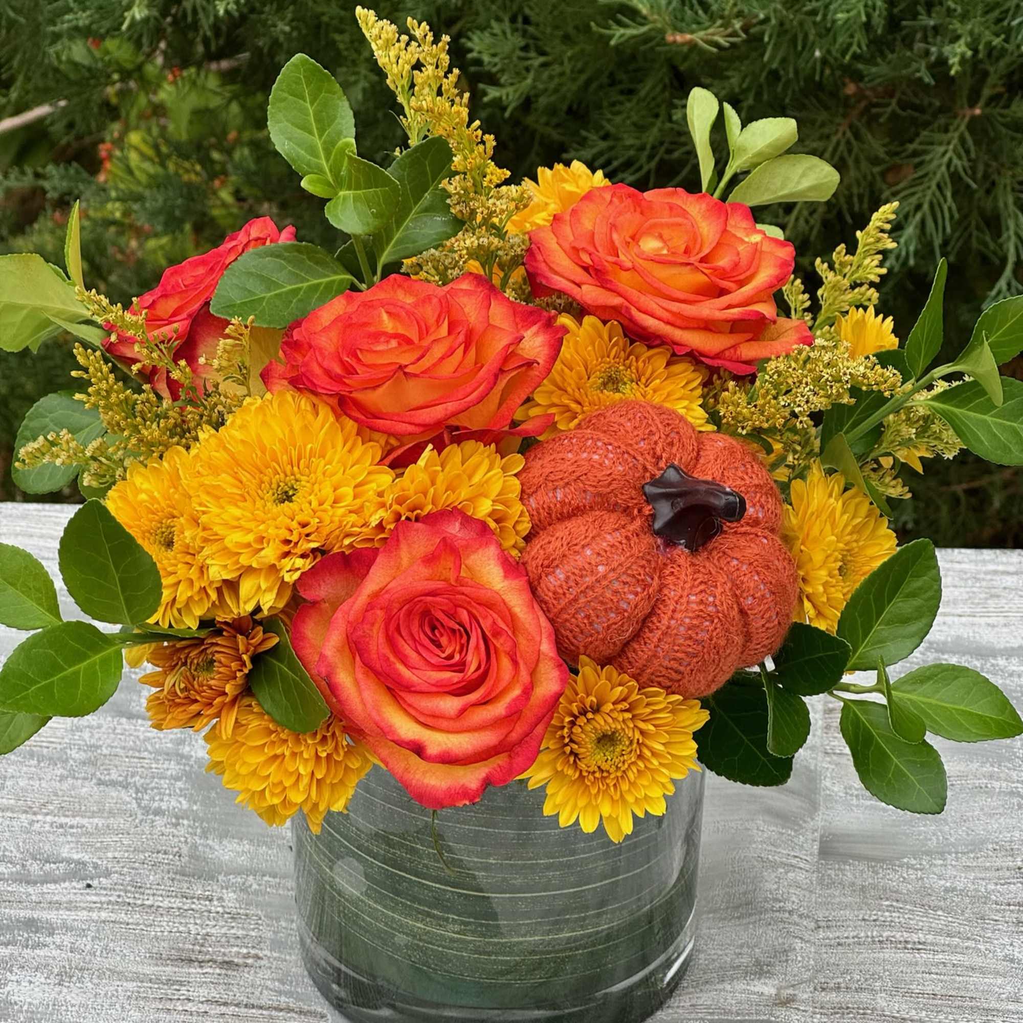 Orange roses and yellow mums in a glass vase with a small pumpkin accent