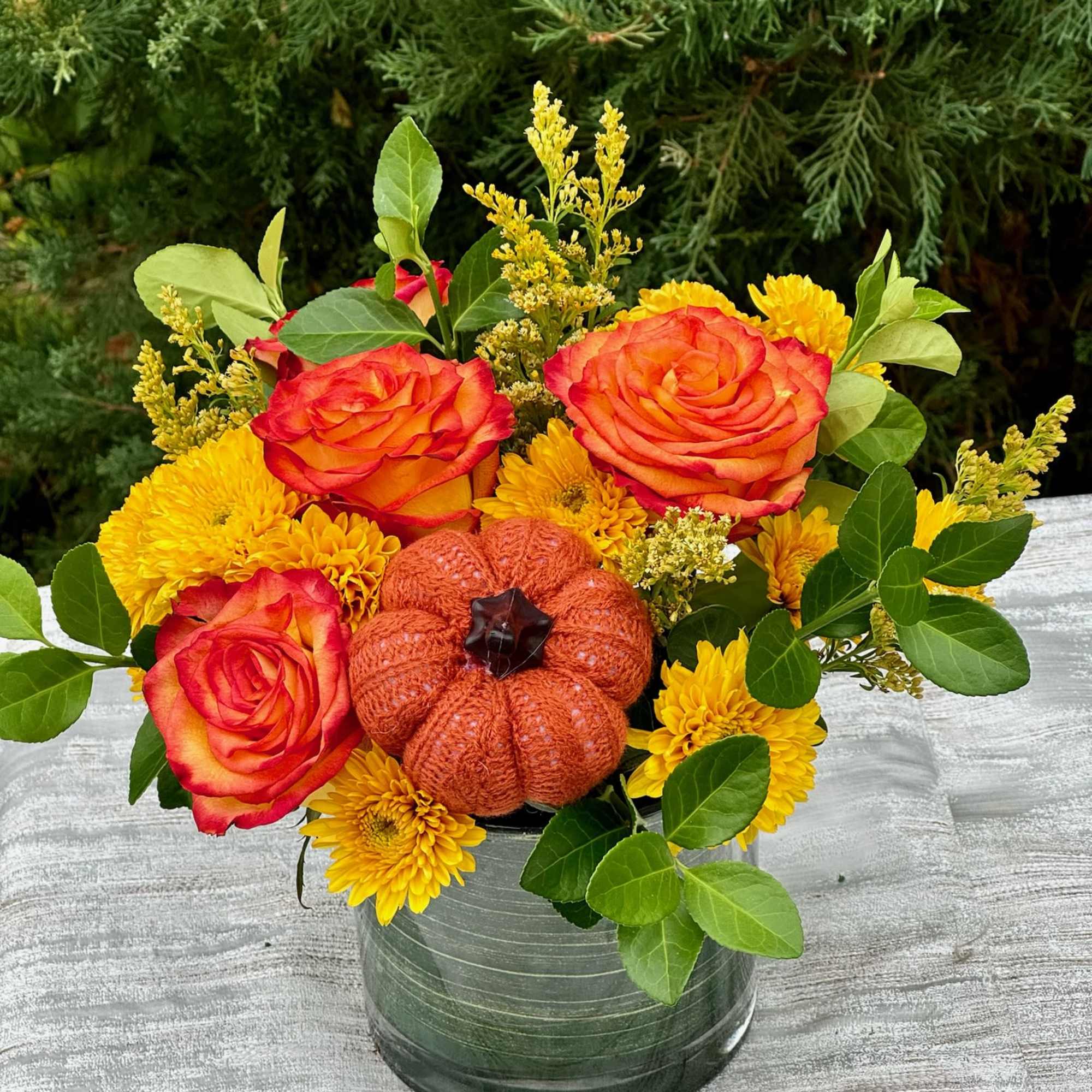 Orange roses and yellow mums in a glass vase with a small pumpkin accent
