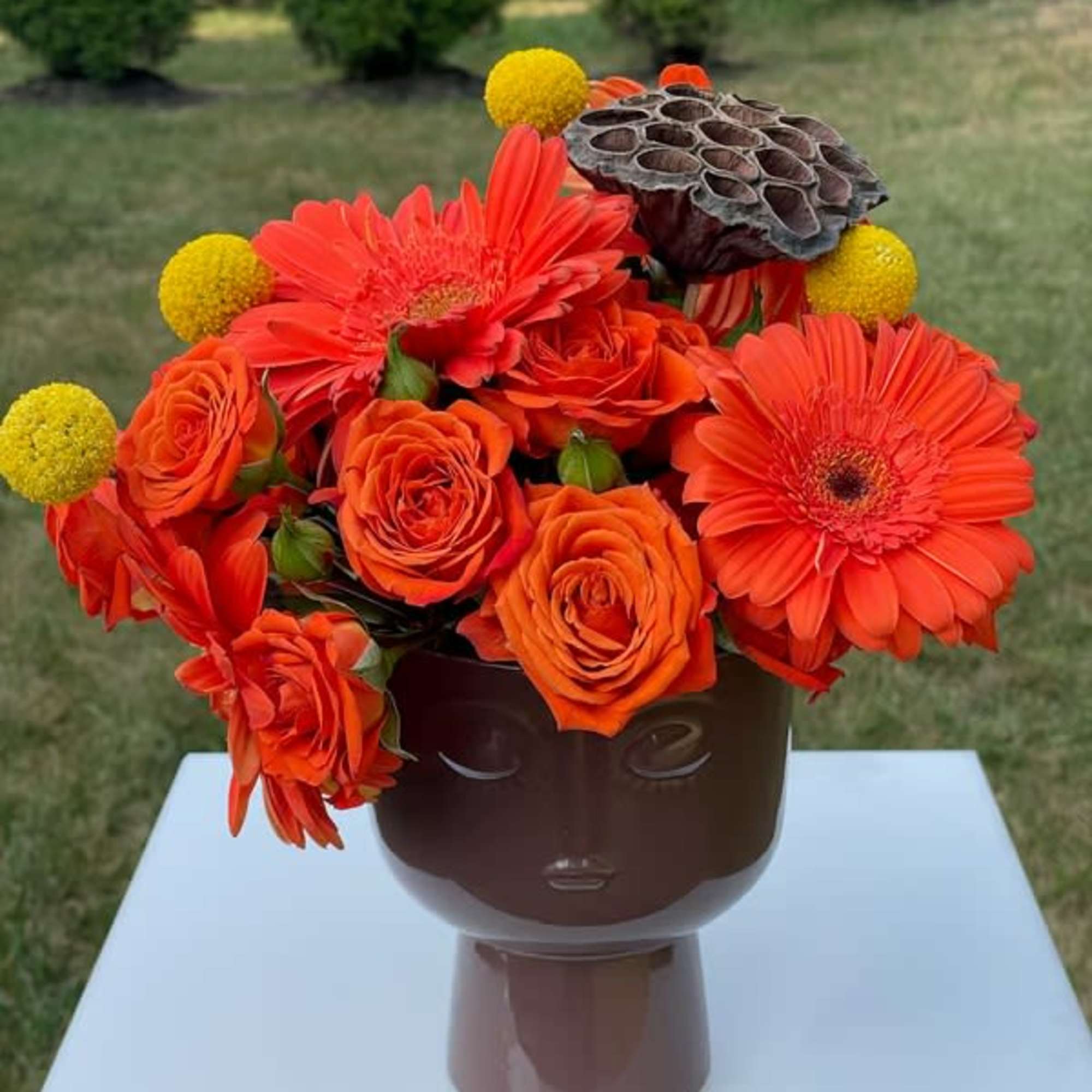 Orange roses and gerbera daisies in a brown face vase