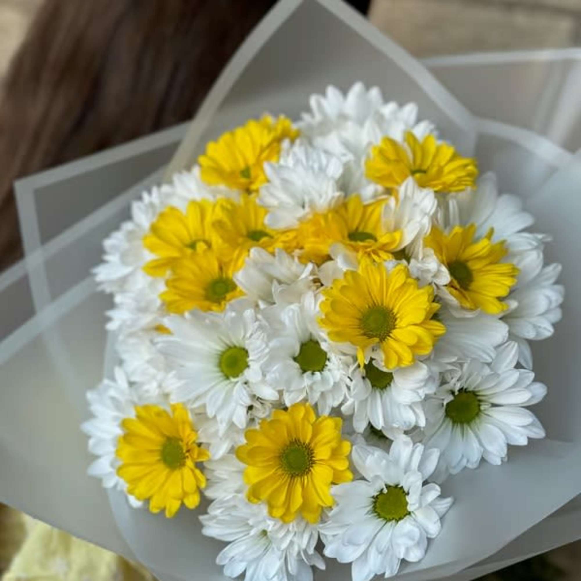Bouquet of yellow and white daisies wrapped in gray paper