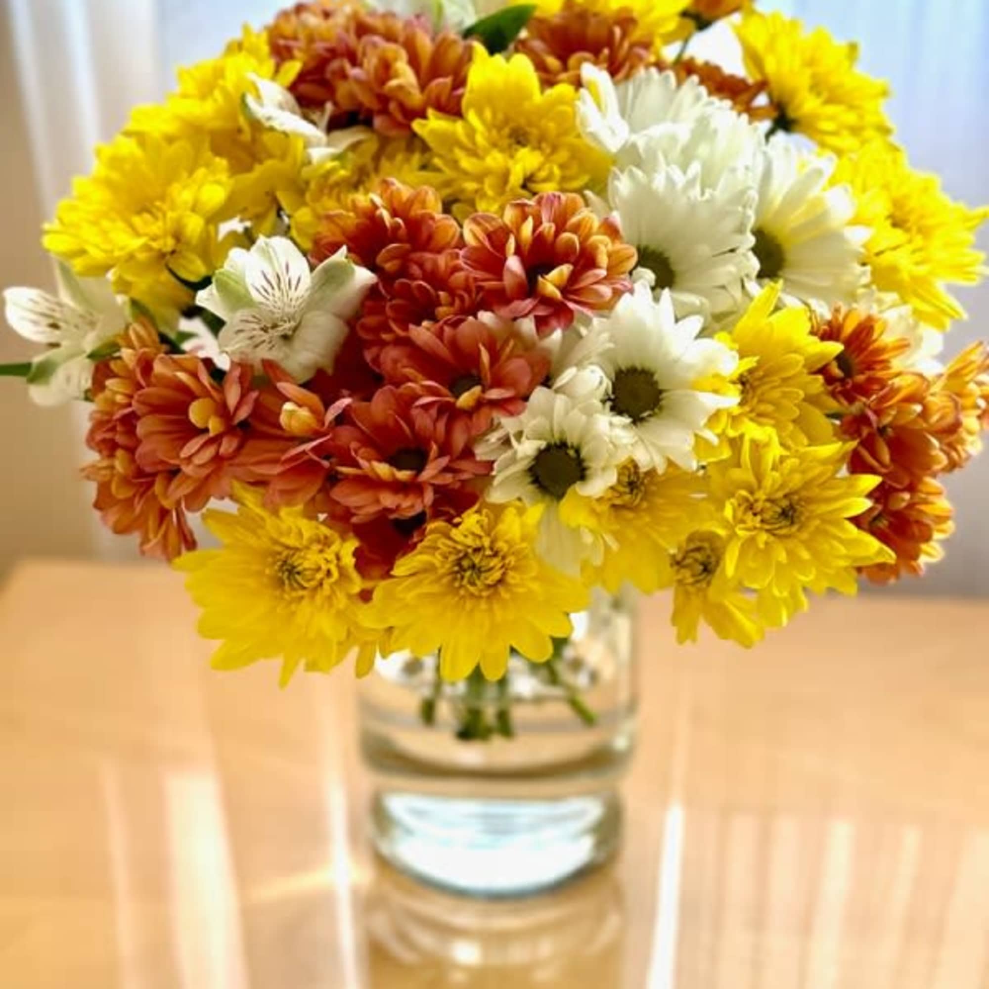 Bouquet of yellow, white, and orange daisies in a clear glass vase