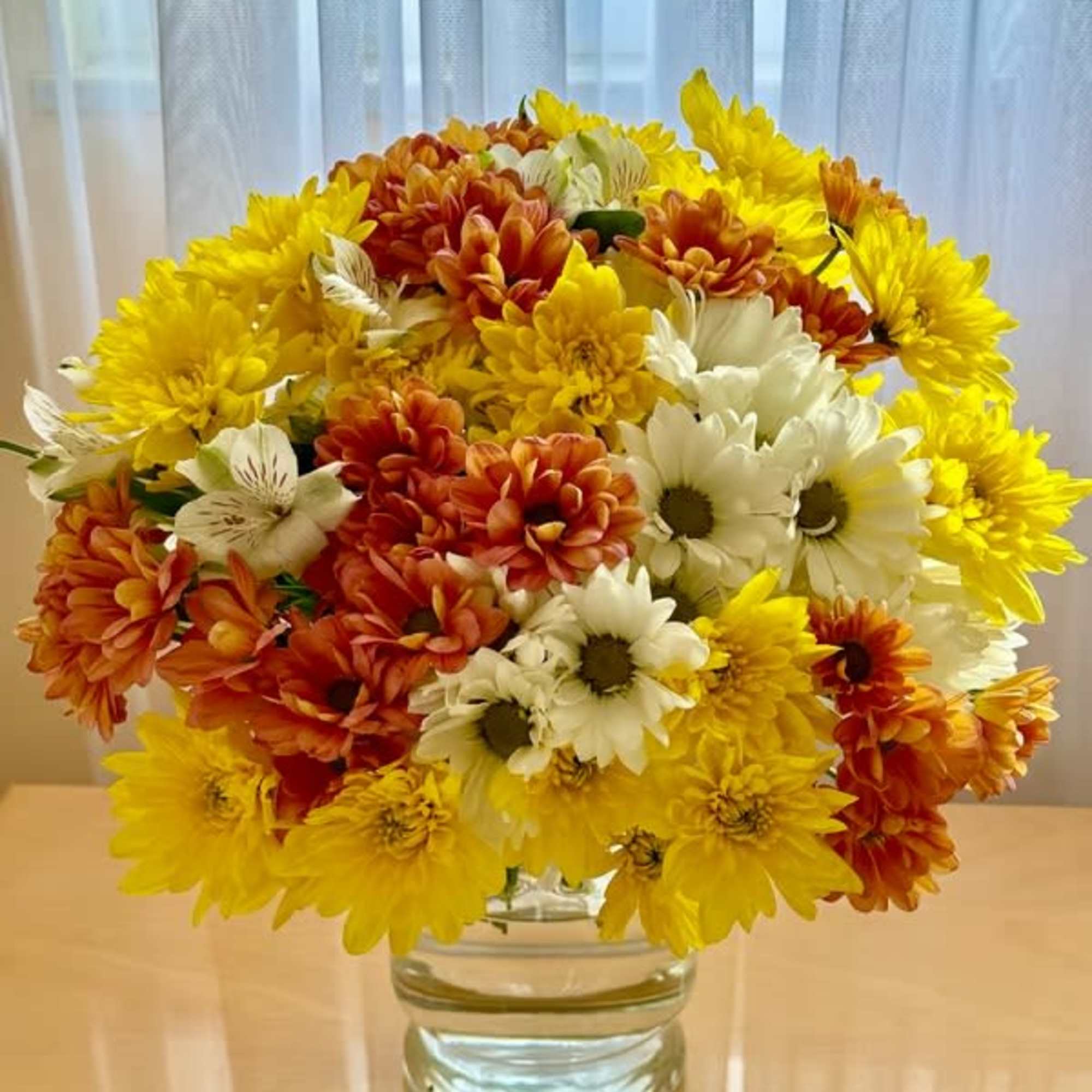 Bouquet of yellow, orange, and white daisies in a clear glass vase
