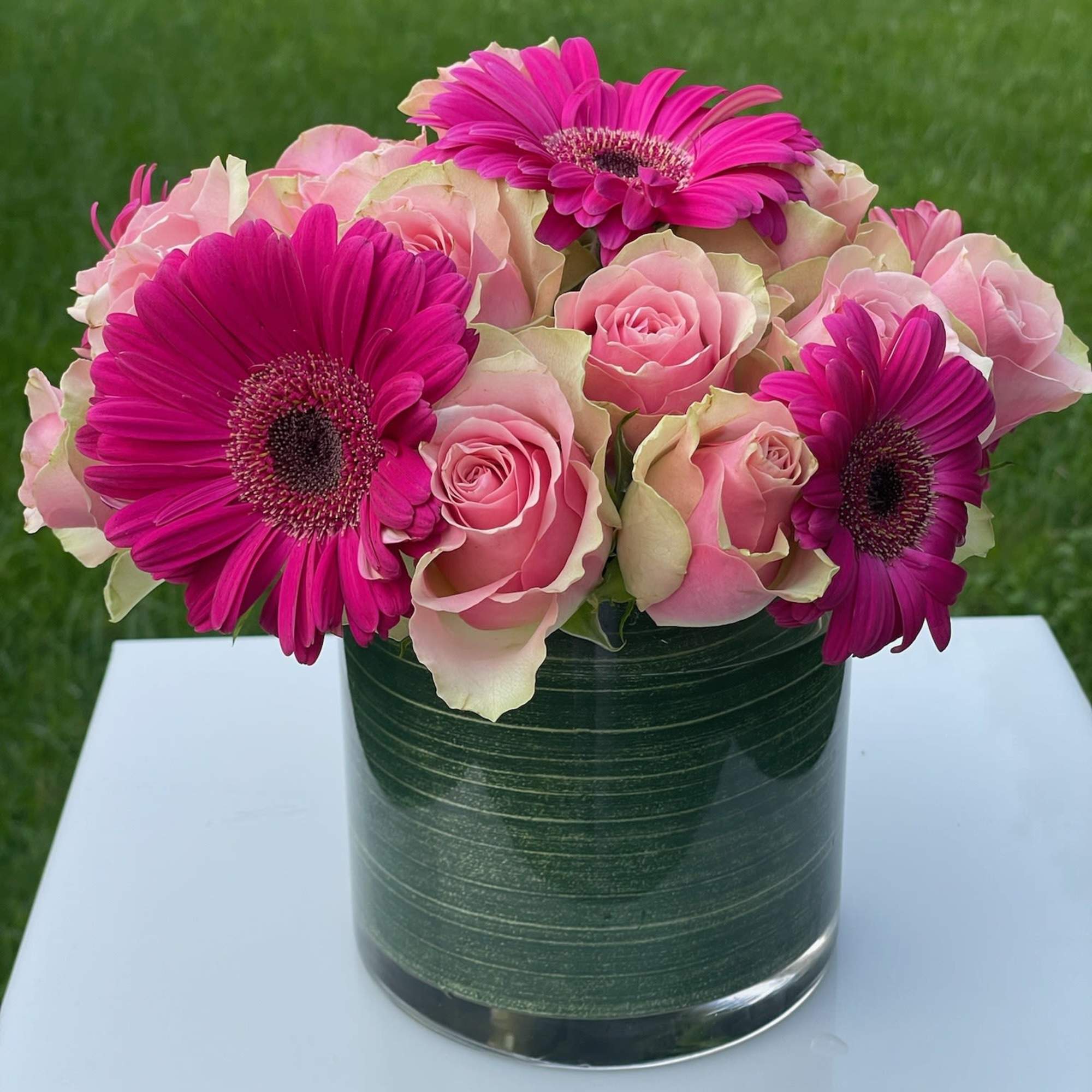 Pink roses and magenta gerbera daisies arranged in a glass vase