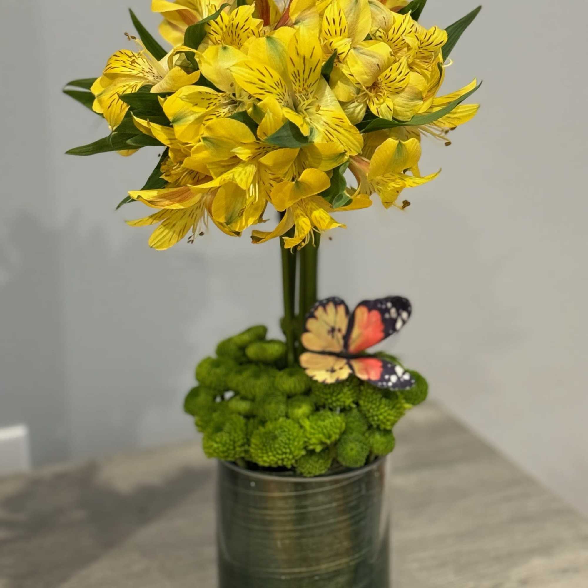 Yellow alstroemeria arrangement in a glass vase with green moss and a butterfly decoration