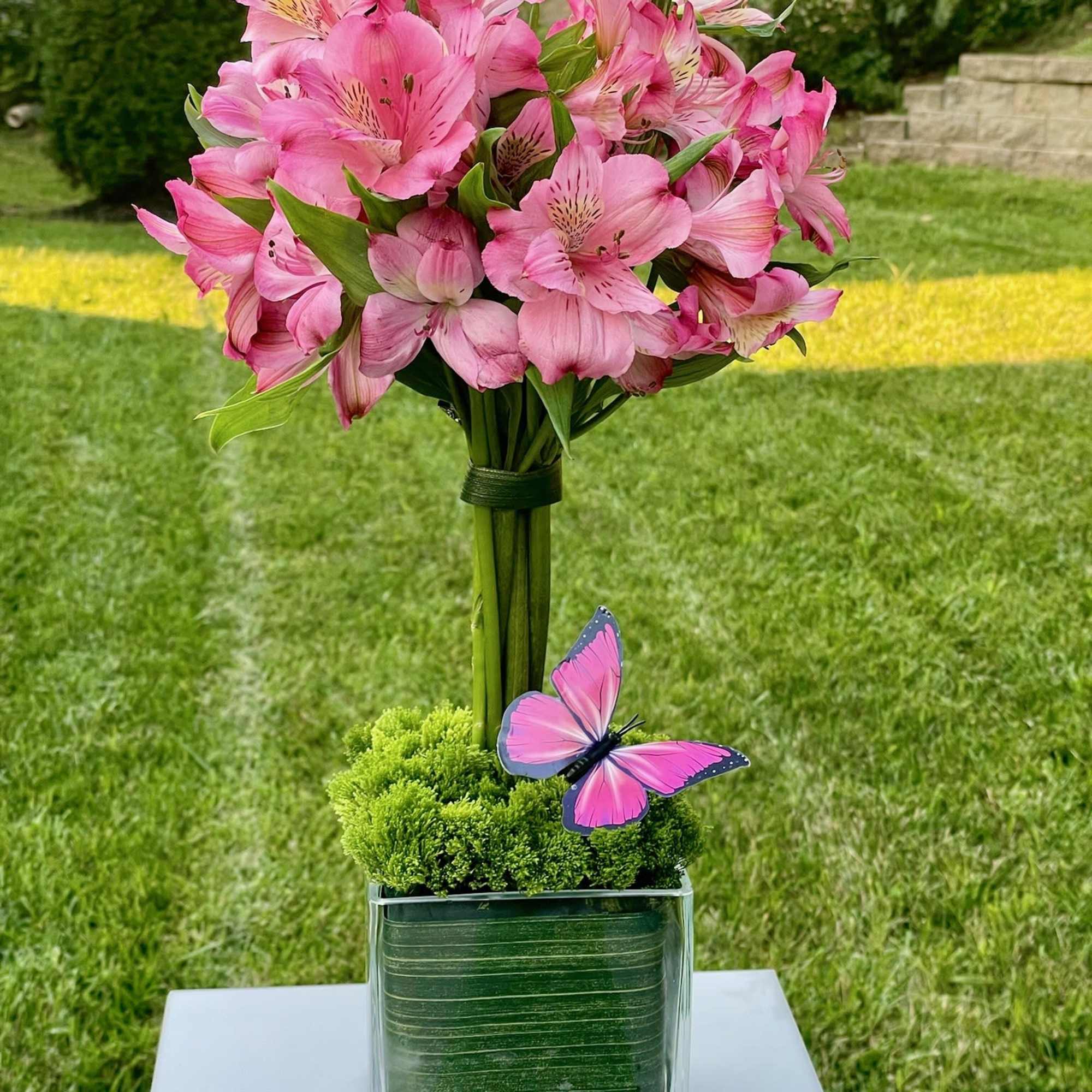 Pink alstroemeria bouquet in a clear square vase with a butterfly accent