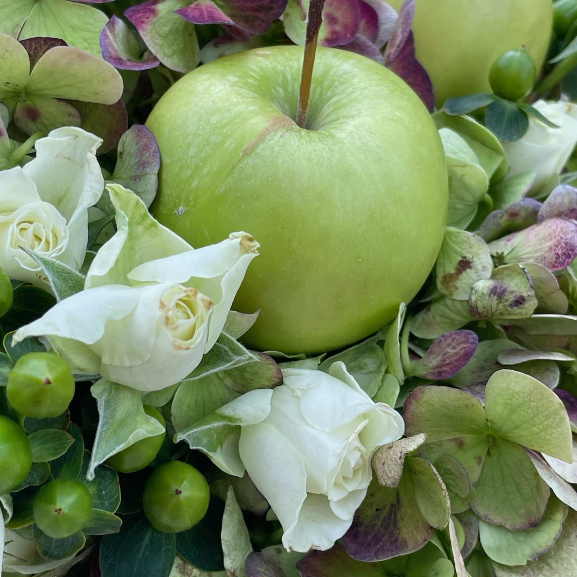 Green apple surrounded by white roses and green-purple hydrangeas