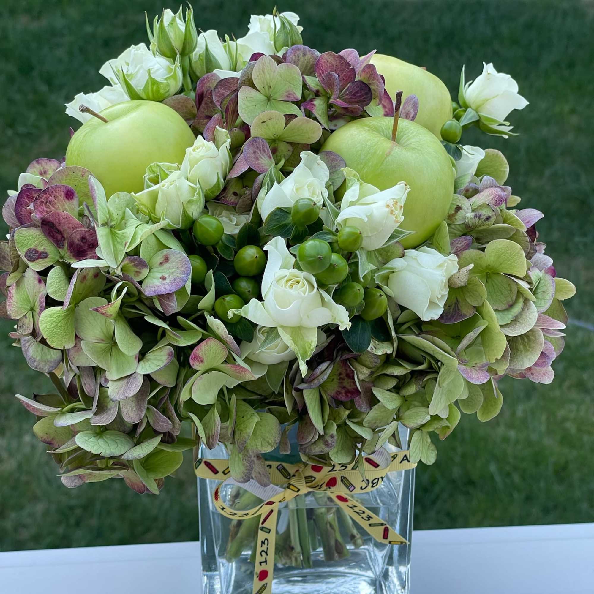 White roses and green hydrangeas in a clear square vase with a ribbon