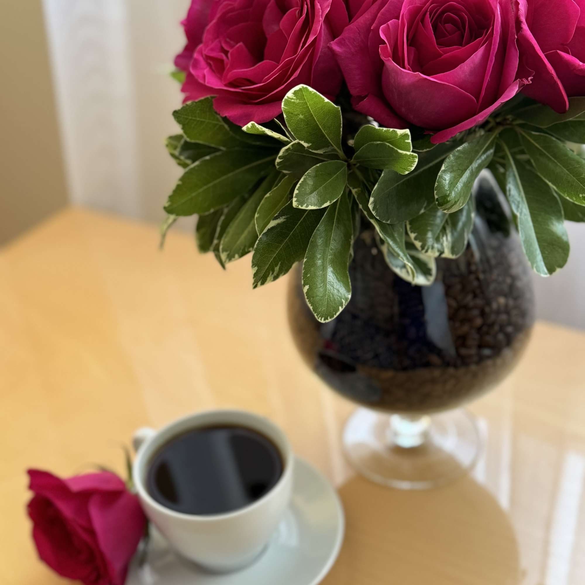 Pink roses in a glass vase beside a cup of coffee