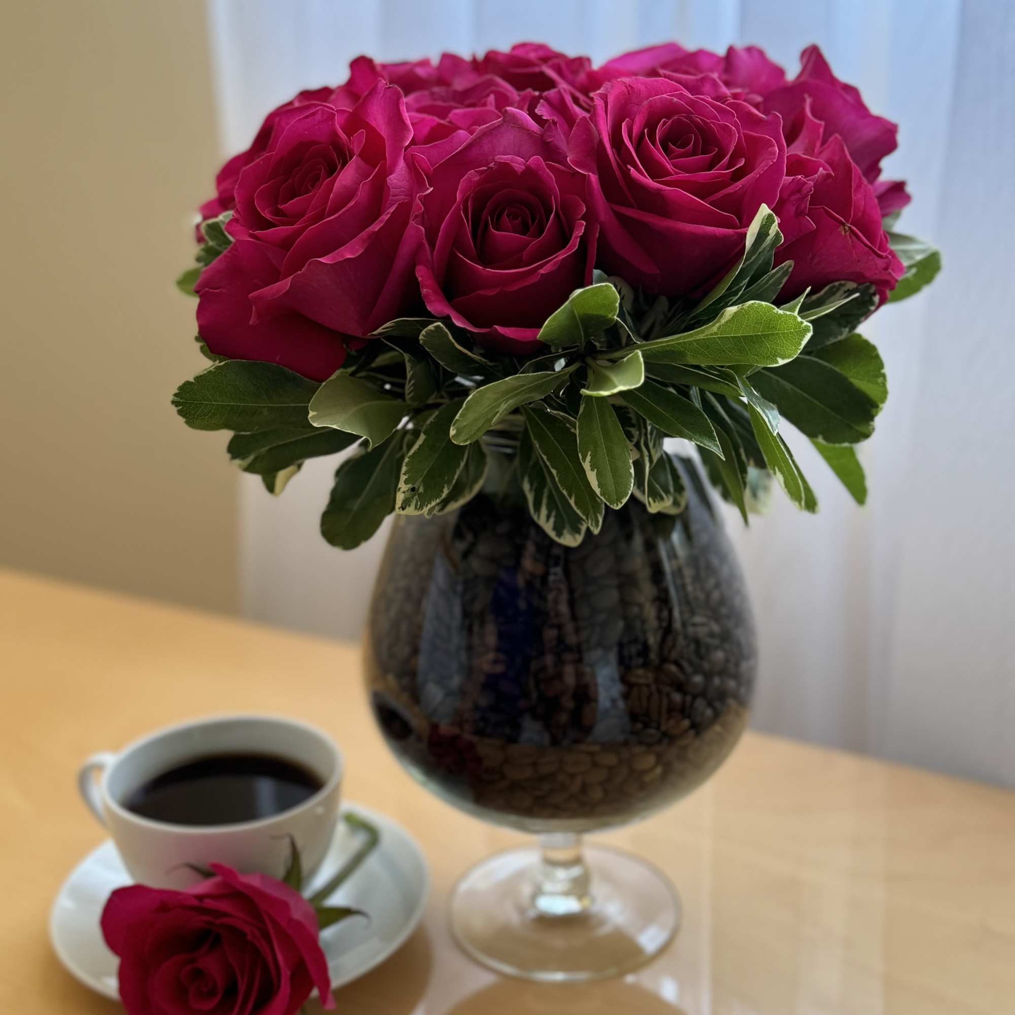Magenta roses arranged in a dark glass vase with a single rose on a saucer