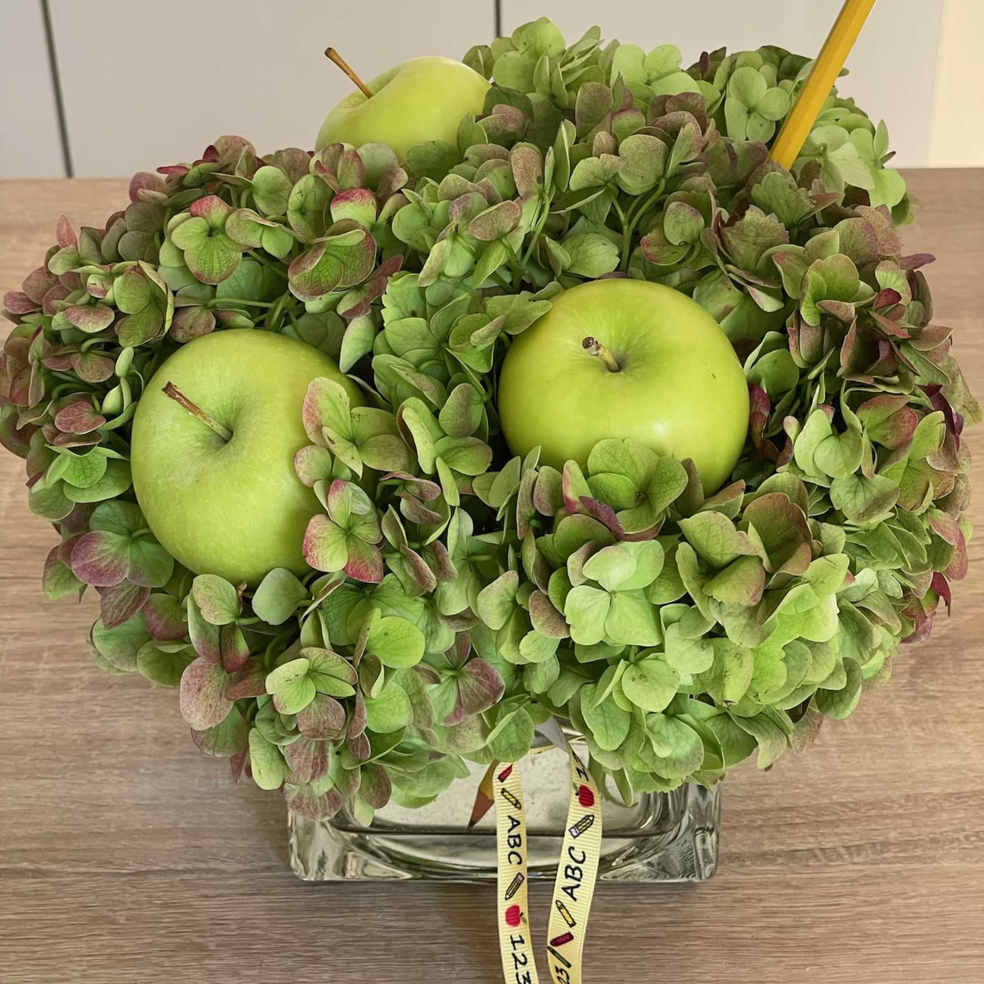 Green hydrangea arrangement with three green apples in a glass vase