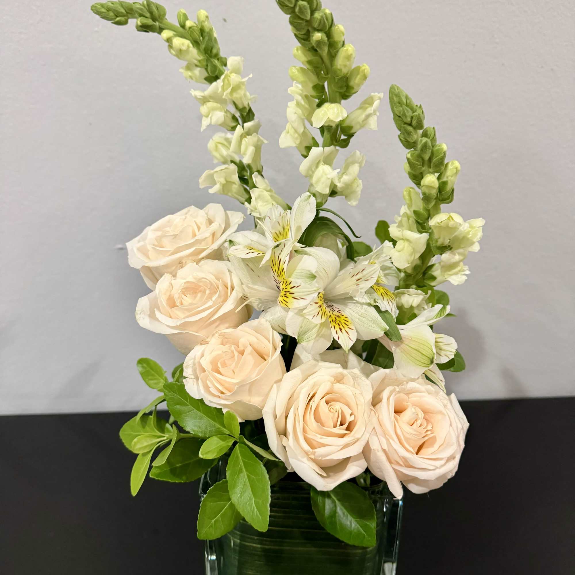 Peach roses and white flowers in a square glass vase